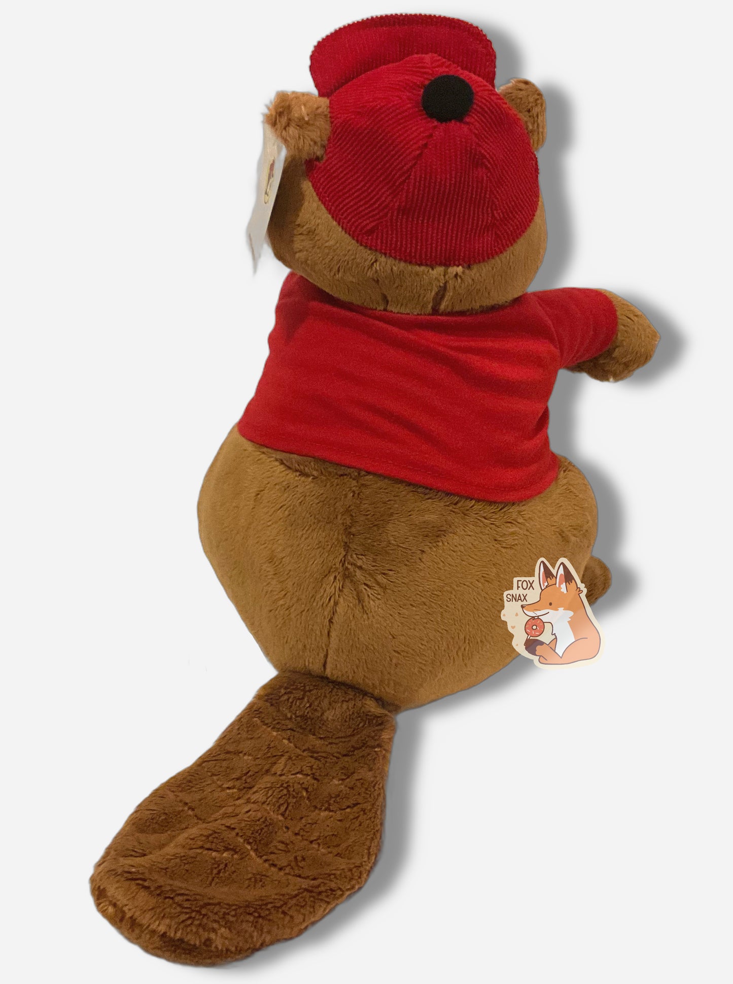 A picture of the back of an adorable Buc-ee the Beaver plush. The plush is of Buc-ee, wearing a red Buc-ee's shirt and red ball cap, and is looking to the left. Buc-ee has a large brown fuzzy beaver tail, and is covered in plush brown and white stuffed animal "fur".