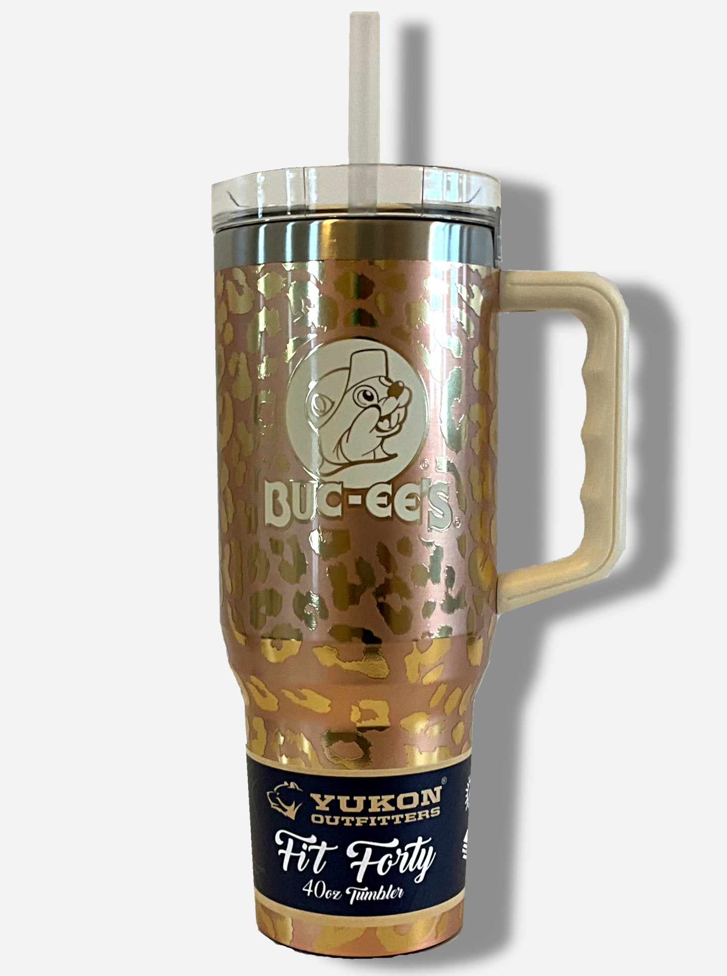 A picture of a tall, gold, sorta skinny tumbler, with a big picture of Buc-ee The Beaver on it. The surface is a leopard print, as it is gold paint covering stainless steel. The handle, top, and straw are plastic. The top of the mug is lined with a stainless steel band. A paper wrapper around the bottom reads: Yukon Outfitters. Fit Forty 40 oz Tumbler.