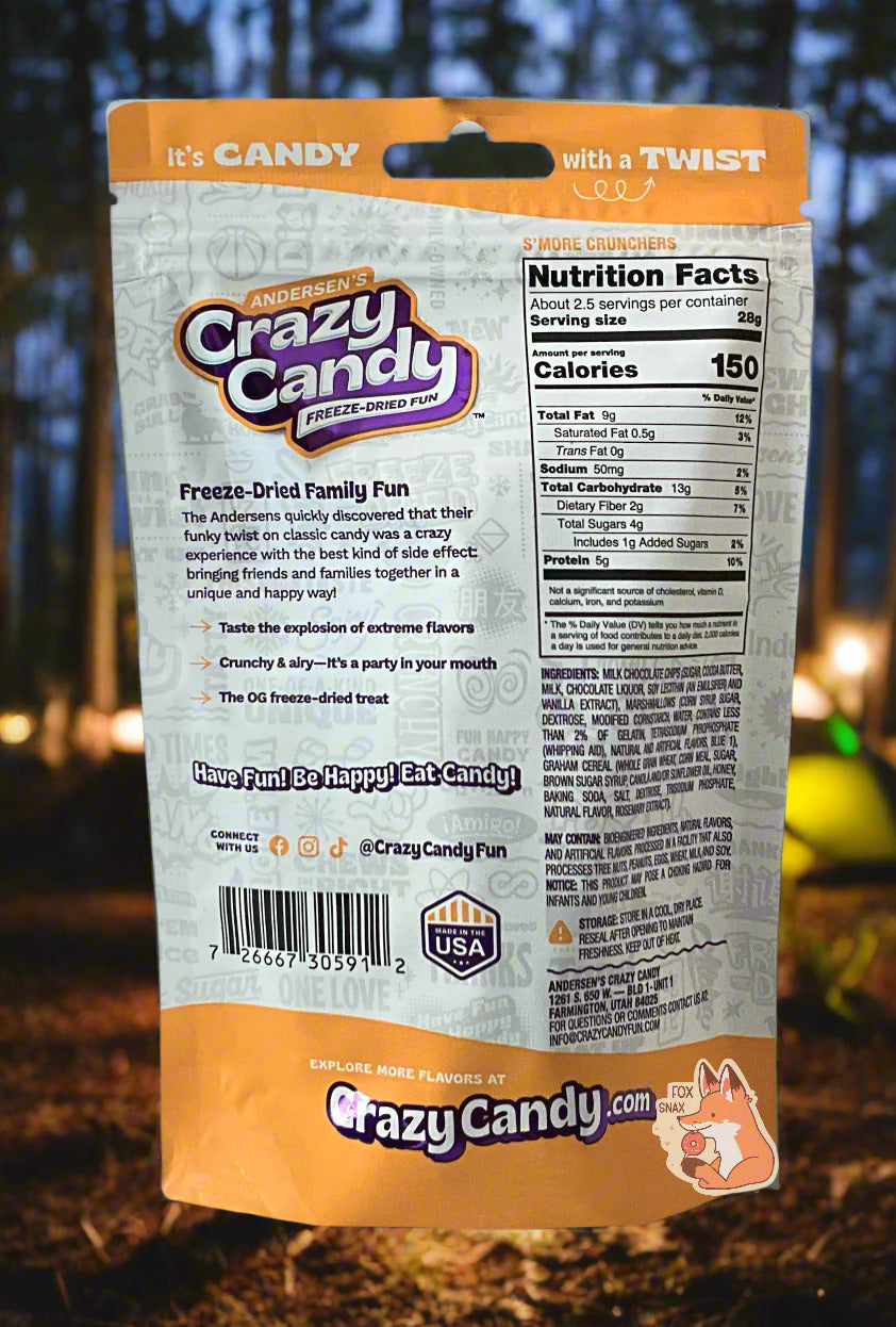 The back of a large bag of Andersen's Crazy Candy S'more Crunchers. The bag reads: Freeze Dried Family Fun. The Andersens quickly discovered that their funky twist on classic candy was a crazy experience with the best kind of side effect: bringing friends and families together in a unique and happy way! The background shows a forest and several tents in a campground.