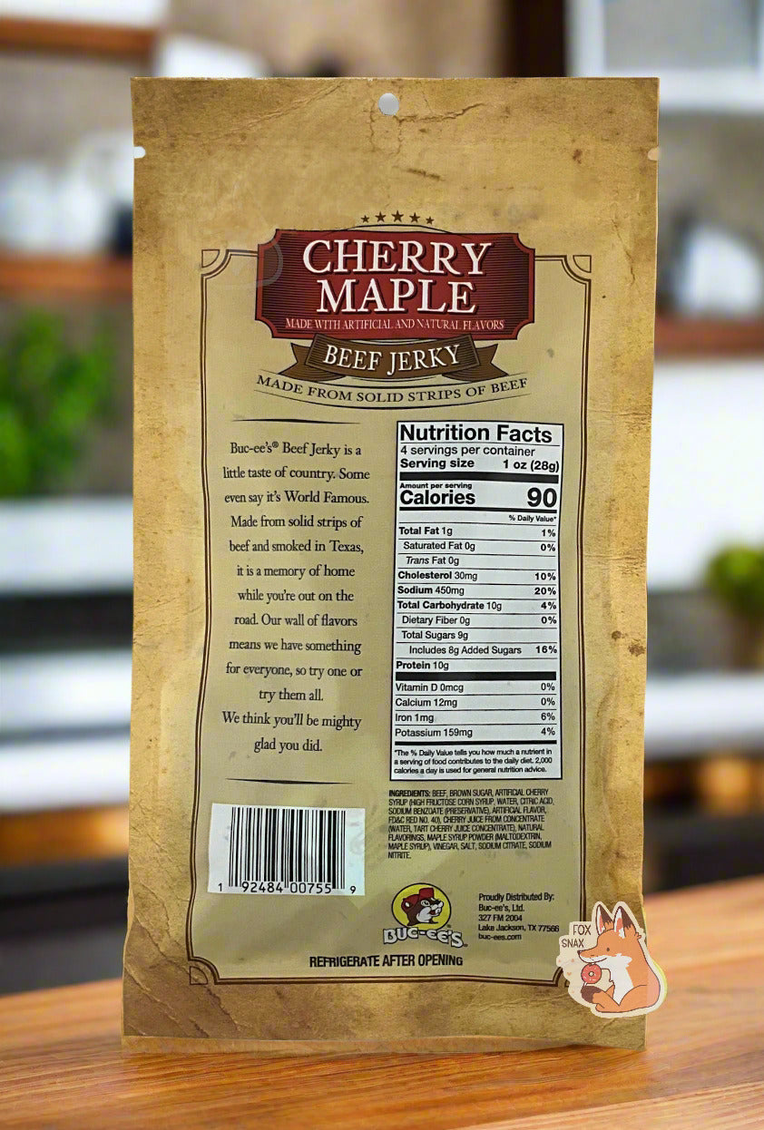 A picture of the back of a tan plastic bag of Buc-ee's Cherry Maple Beef Jerky. The label underneath reads 'Buc-ee's Beef Jerky is a little taste of country. Some even say it's World Famous. Made from solid strips of beef and smoked in Texas, it is a memory of home while you're out on the road. Our wall of flavors means we have something for everyone, so try one or try them all. We think you'll be mighty glad you did.' The background is of a fancy, wood paneled kitchen with green plants.