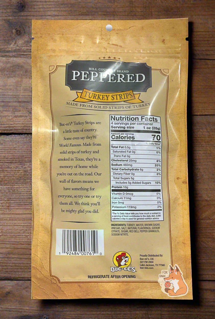 A picture of the back of a bag of Buc-ee's Hill Country Brand Peppered Turkey Strips. The label reads 'Made From Solid Strips Of Turkey' then 'Buc-ee's Turkey Strips are a little taste of country. Some even say it's World Famous. Made from solid strips of turkey and smoked in Texas, it is a memory of home while you're out on the road. Our wall of flavors means we have something for everyone, so try one or try them all. We think you'll be mighty glad you did.' The bag sits on a rough wooden table.