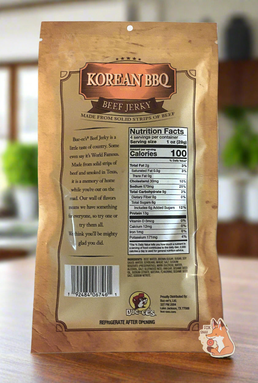 A picture of the back of a tan plastic bag of Buc-ee's Korean BBQ Beef Jerky.  The label underneath reads 'Buc-ee's Beef Jerky is a little taste of country.  Some even say it's World Famous.  Made from solid strips of beef and smoked in Texas, it is a memory of home while you're out on the road.  Our wall of flavors means we have something for everyone, so try one or try them all.  We think you'll be mighty glad you did.'  The background is a dark wood paneled kitchen with green plants  in the background