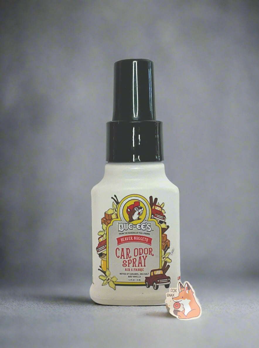 Front of a white bottle of Buc-ee's car odor spray on a white background. The label reads Beaver Nuggets Car Odor Spray, Air & Fabric, Notes of Caramel, Sea Salt, and Vanilla, then 1.4 FL OZ. The text is surrounded by the Buc-ee's logo, vanilla flowers, caramels, red trucks, and vanilla beans. The background is grey and white.