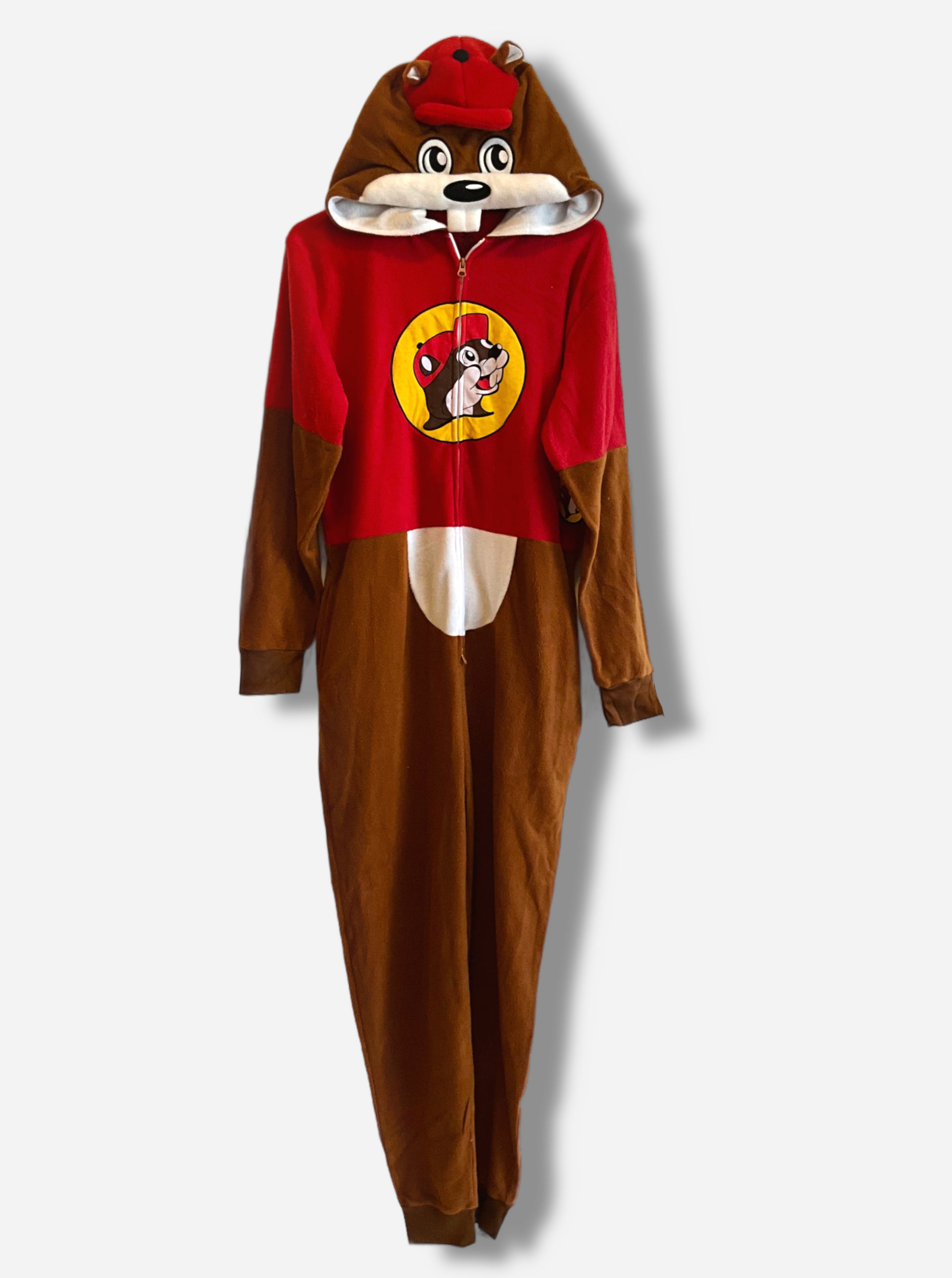 A picture of a large onesie that resembles Buc-ee The Beaver.  The hood is Buc-ee's beaver head, complete with fuzzy brown ears, adorable eyes, and red ball cap.  A pair of white beaver teeth is present on the top of the hood.  The chest of the hoodie has a zipper down the front, and is colored like a red Buc-ee's shirt, complete with the Buc-ee's logo on it.  The legs and arms are brown cloth "fur", and a white belly can be seen.