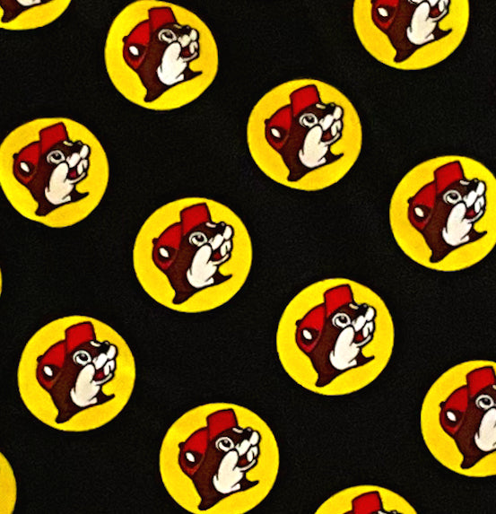 A closeup of a picture of a pair of black pants. The pants are covered in Buc-ee's logos: a grinning beaver wearing a red ballcap, backlit by a yellow circle.