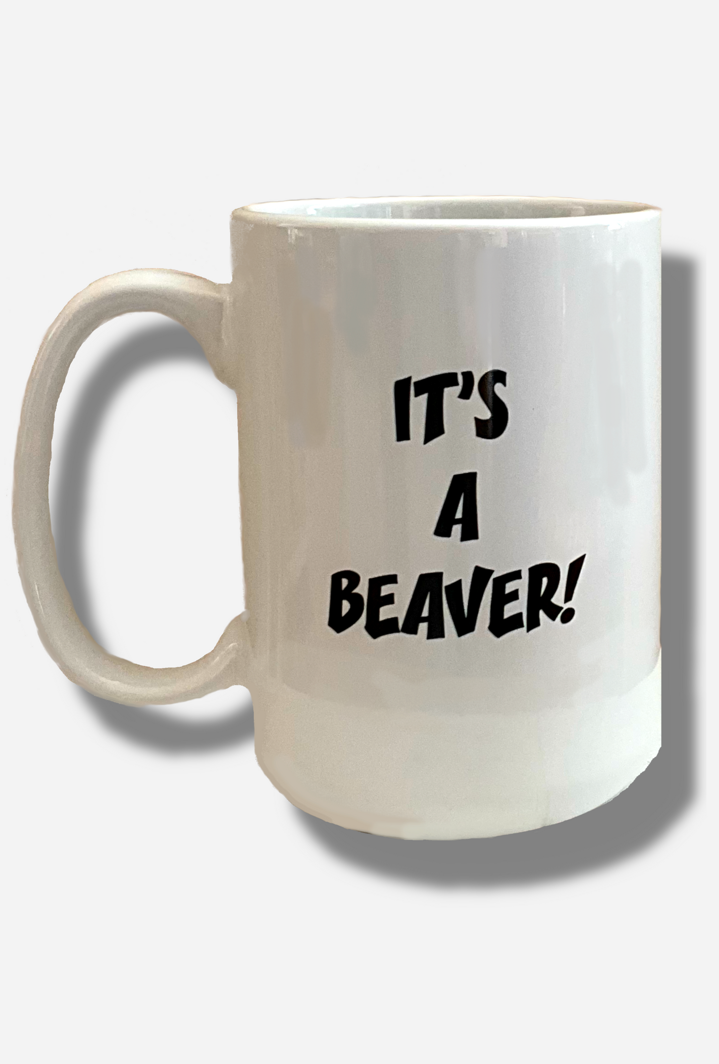A picture of the back of a white ceramic coffee mug, with a white handle. The middle of the mug reads IT'S A BEAVER! in a jolly font.