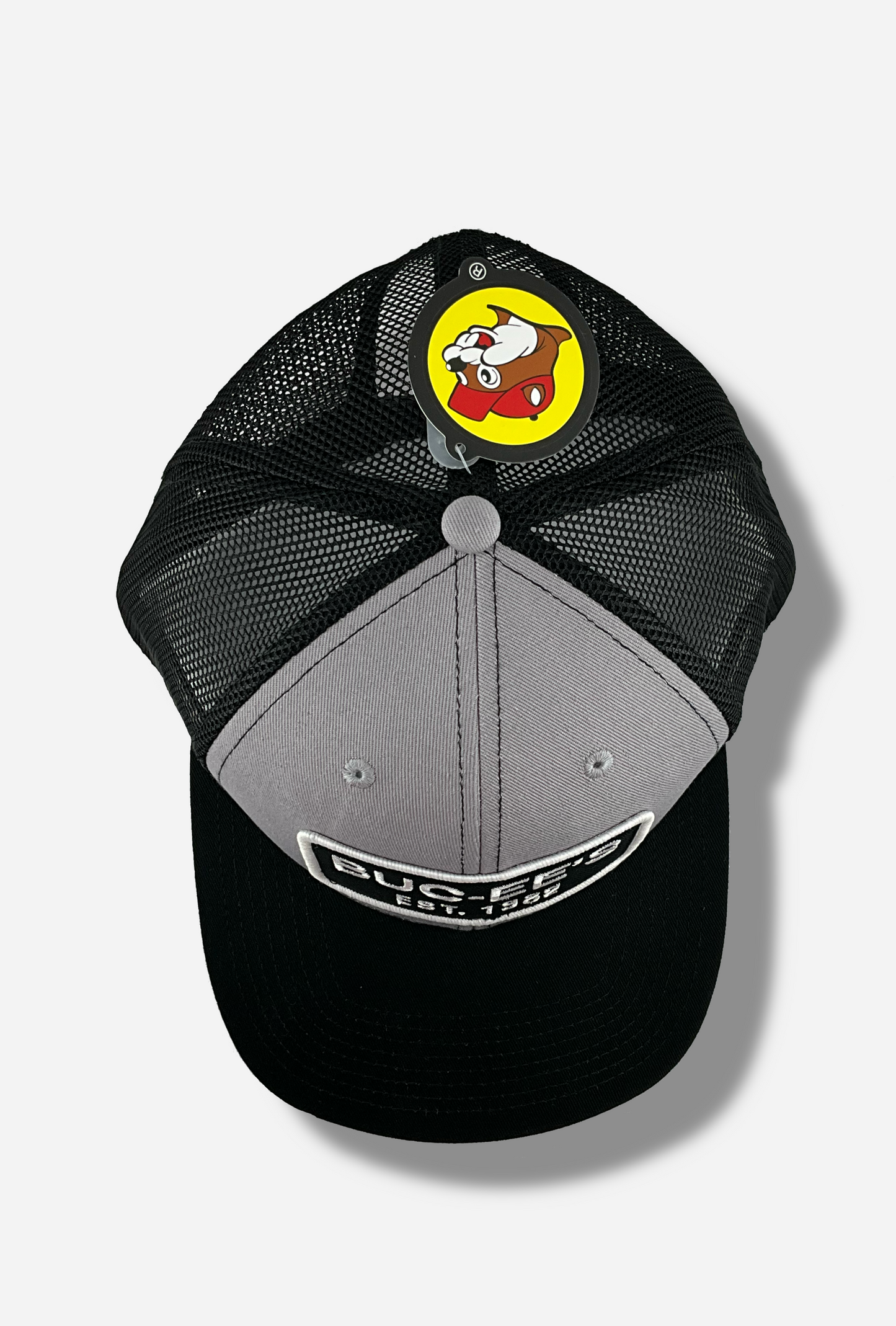 A picture of the top of a grey and black ball cap. The front of the cap is grey, and has a large white and black rectangular patch that reads BUC-EE'S, and underneath that, EST. 1982. The brim of the cap is black. The back and sides of the cap are a black plastic mesh.