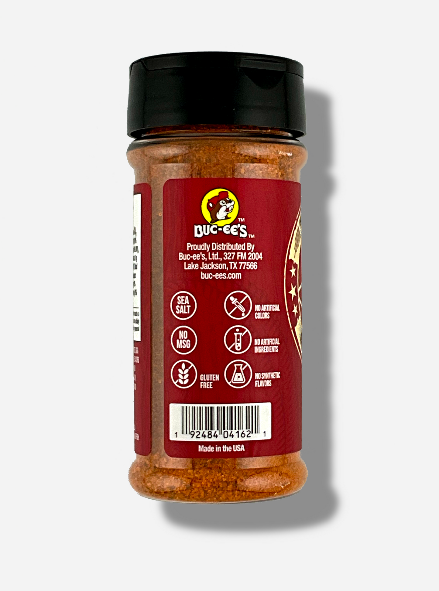 A picture of the side of a container of Texas Round Up BBQ Rub. The container has a black plastic flip lid, and a clear plastic body. The spices inside appear red/orange and black. The red label reads SEA SALT, NO MSG, GLUTEN FREE, NO ARTIFICIAL COLORS, NO ARTIFICIAL INGREDIENTS, NO SYNTHETIC FLAVORS. Beneath that, MADE IN THE USA