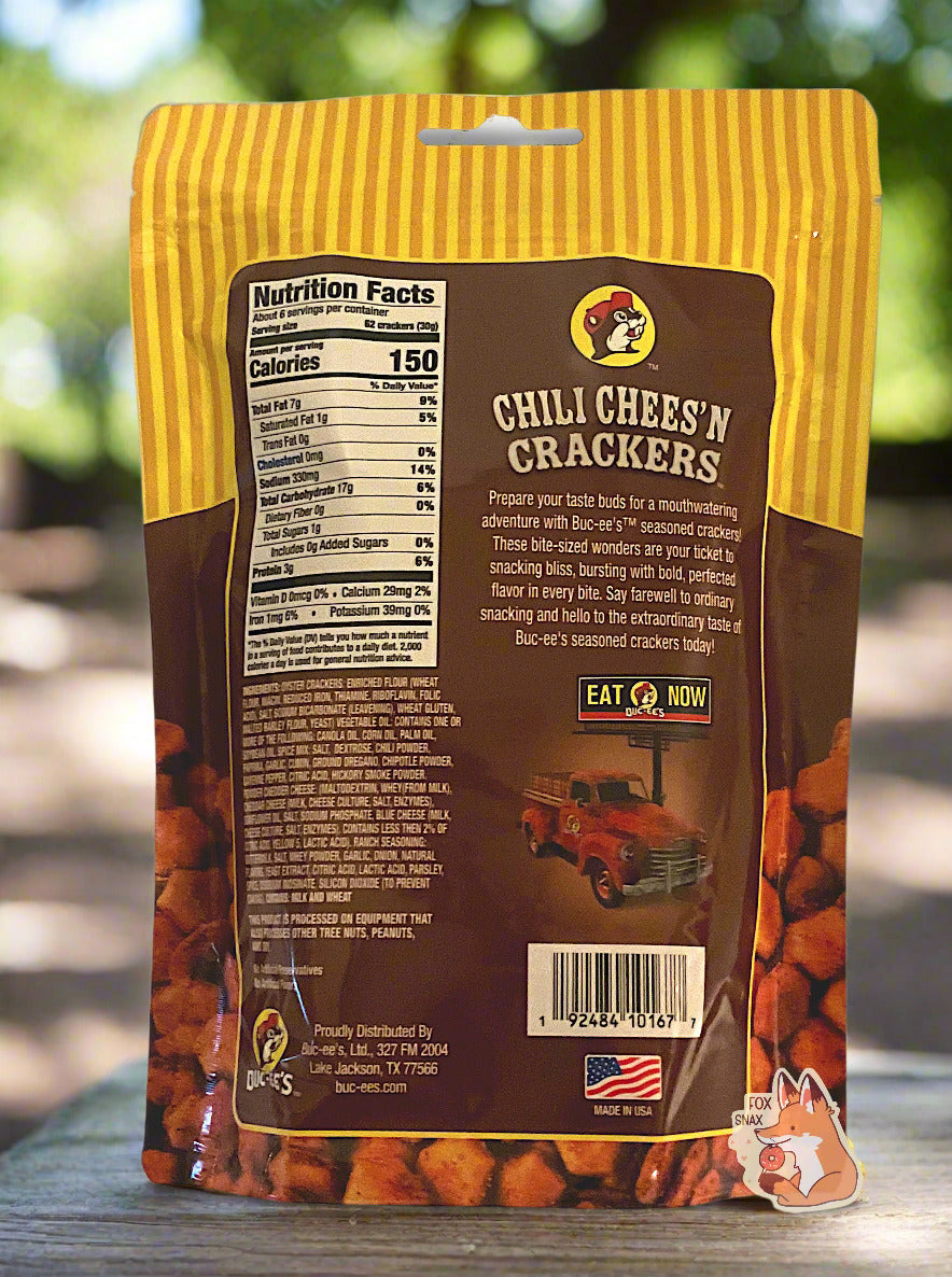 A picture of a the back of a metallic bag of Buc-ee's Chili Cheese'N Crackers. It reads "Prepare your taste buds for a mouthwatering adventure with Buc-ee's TM seasoned crackers! These bite-sized wonders are your ticket to snacking bliss, bursting with bold, perfected flavor in every bite. Say farewell to ordinary snacking and hello to the extraordinary taste of Buc-ee's seasoned crackers today! The background is of a park on a sunny spring day.