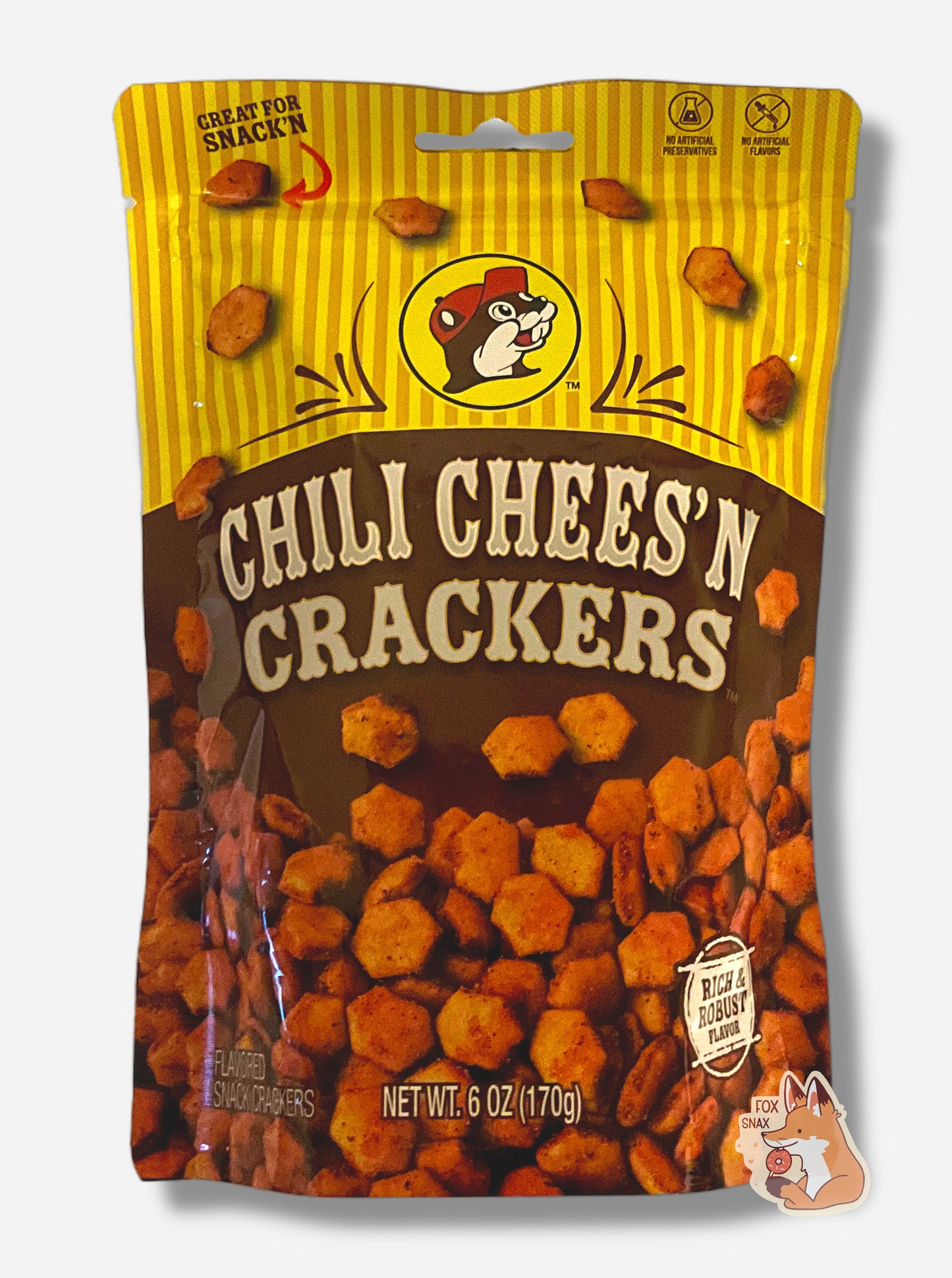 A picture of a metallic bag of Buc-ee's Chili Chees'N Crackers. The logo is a brown-red background on white text; a large number of reddish, savory-looking hexagonal oyster crackers are shown beneath it. At the top is a picture of the logo of Buc-ee The Beaver, and it reads GREAT FOR SNACK'N, NO ARTIFICIAL PRESERVATIVES, FLAVORS and RICH AND ROBUST FLAVOR