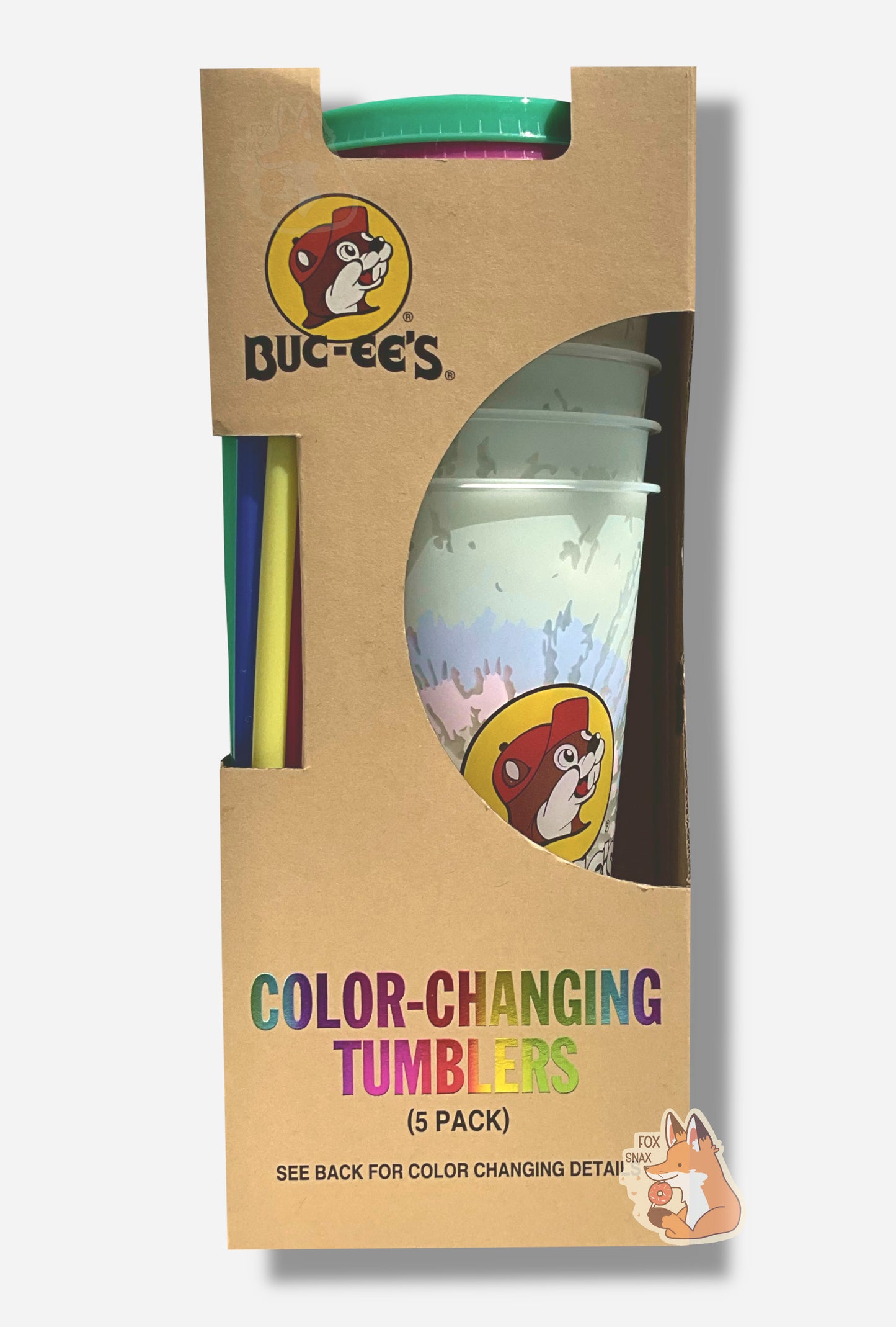 A picture of a tall, thin cardbox box. The bottom of the box reads COLOR-CHANGING TUMBLERS. The top of the box has the Buc-ee's logo. In the middle is a semicircle cut out, which exposes the plastic tumblers. Several tumblers can be seen, and they show a faded, white-ish plastic tumbler with a faint tie-dye pattern through the semicircle. Each of the tumblers is tall, plastic, and has the Buc-ee's logo on it.