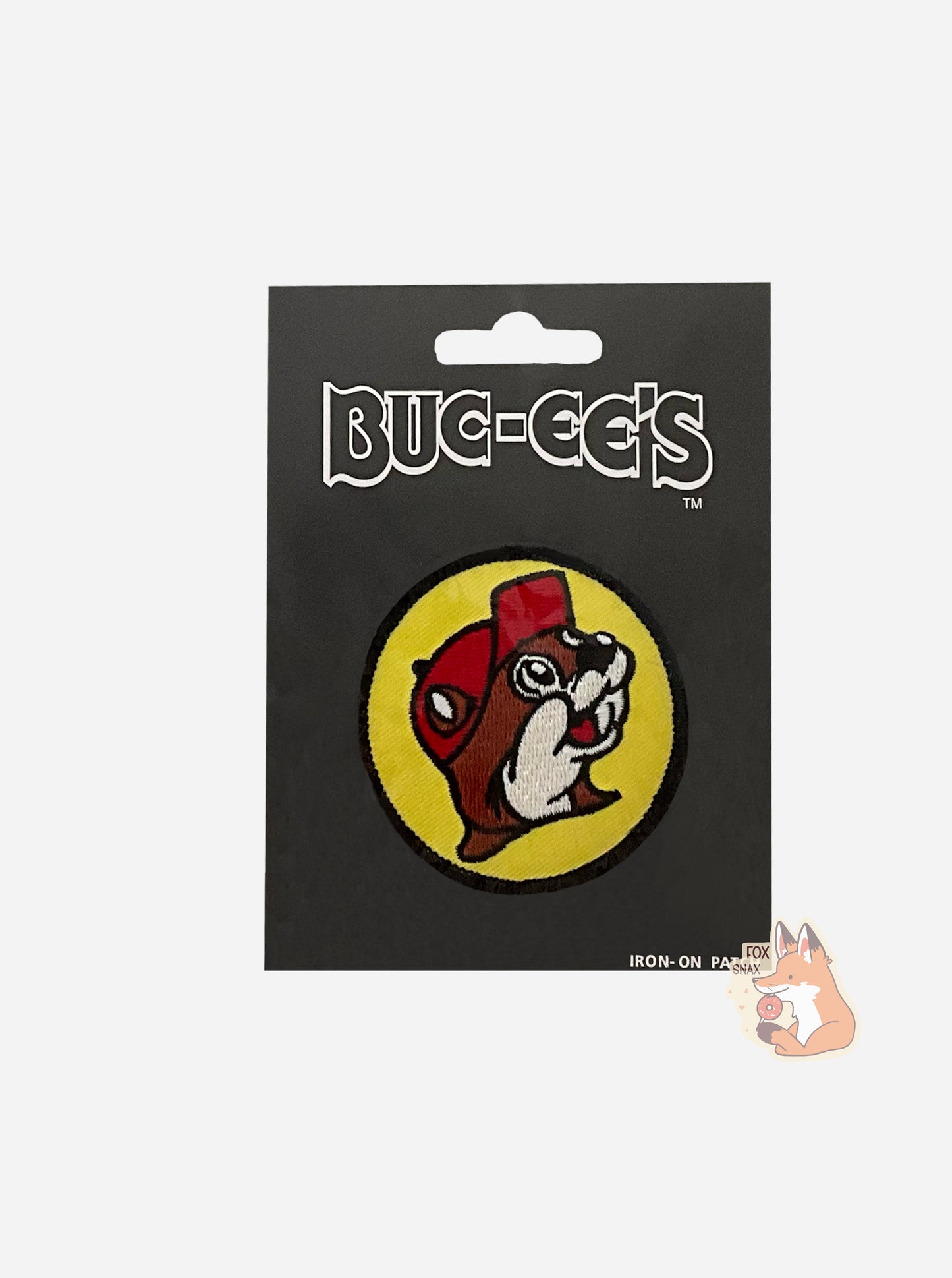 A picture of a circular iron-on patch. The patch is the Buc-ee's logo: a grinning beaver with a significant overbite and brown and white fur, wearing a red ballcap. Buc-ee is surrounded with a yellow circle, which is lined with black.