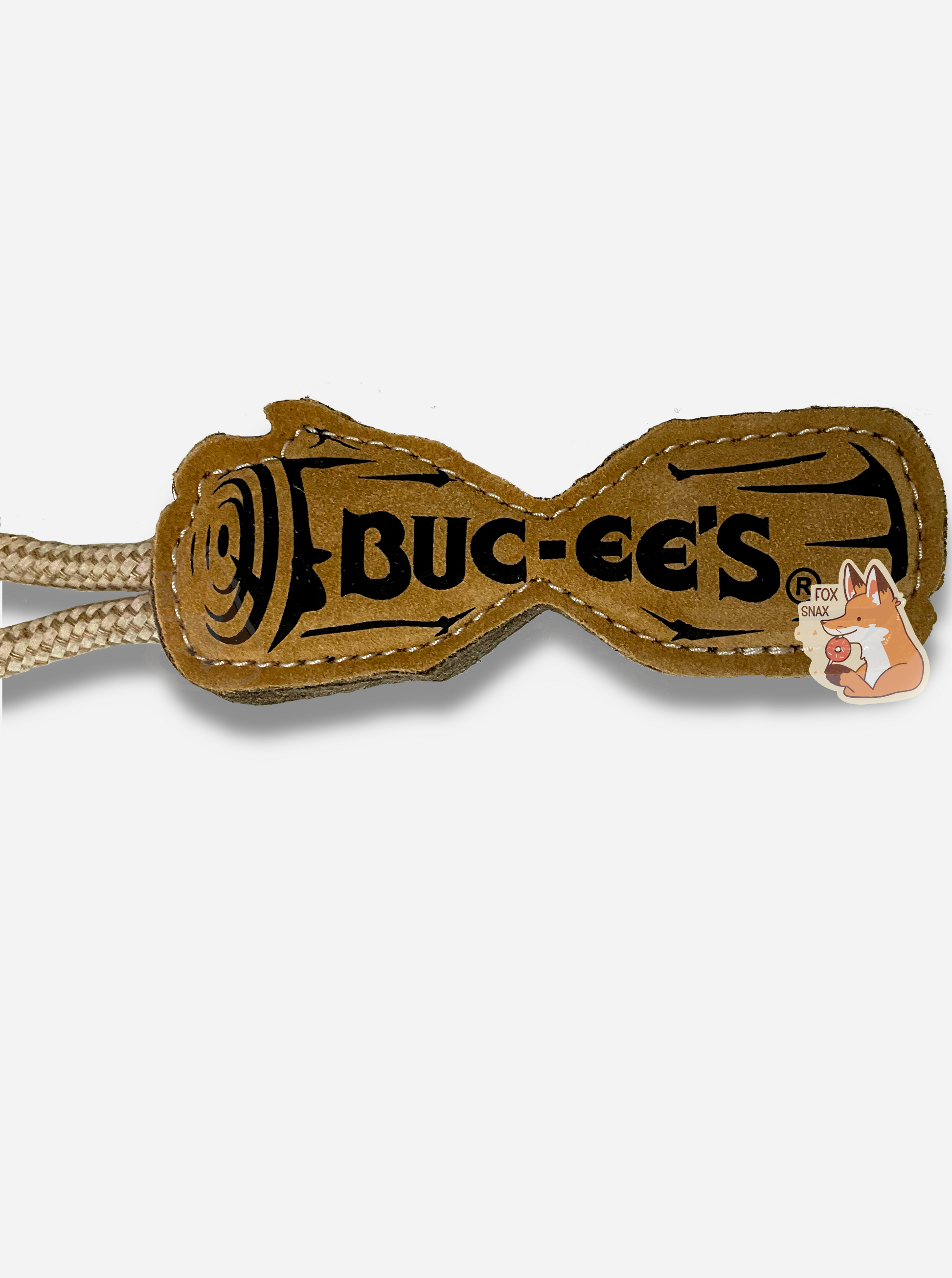 A close up picture of a Buc-ee's "Pet Essentials" Log Rope dog toy.  The body of the toy is shaped like a log - roughly - with a flat body and a dip in the middle, presumably to make it easier for a dog to bite it.  On one end is a strong tan rope.  The body of the tool is tan, and also has a black outline of a log with BUC-EE'S written in the middle.  Both ends of the  rope are tied into one end of the "log", making a loop for a person to hold on to.