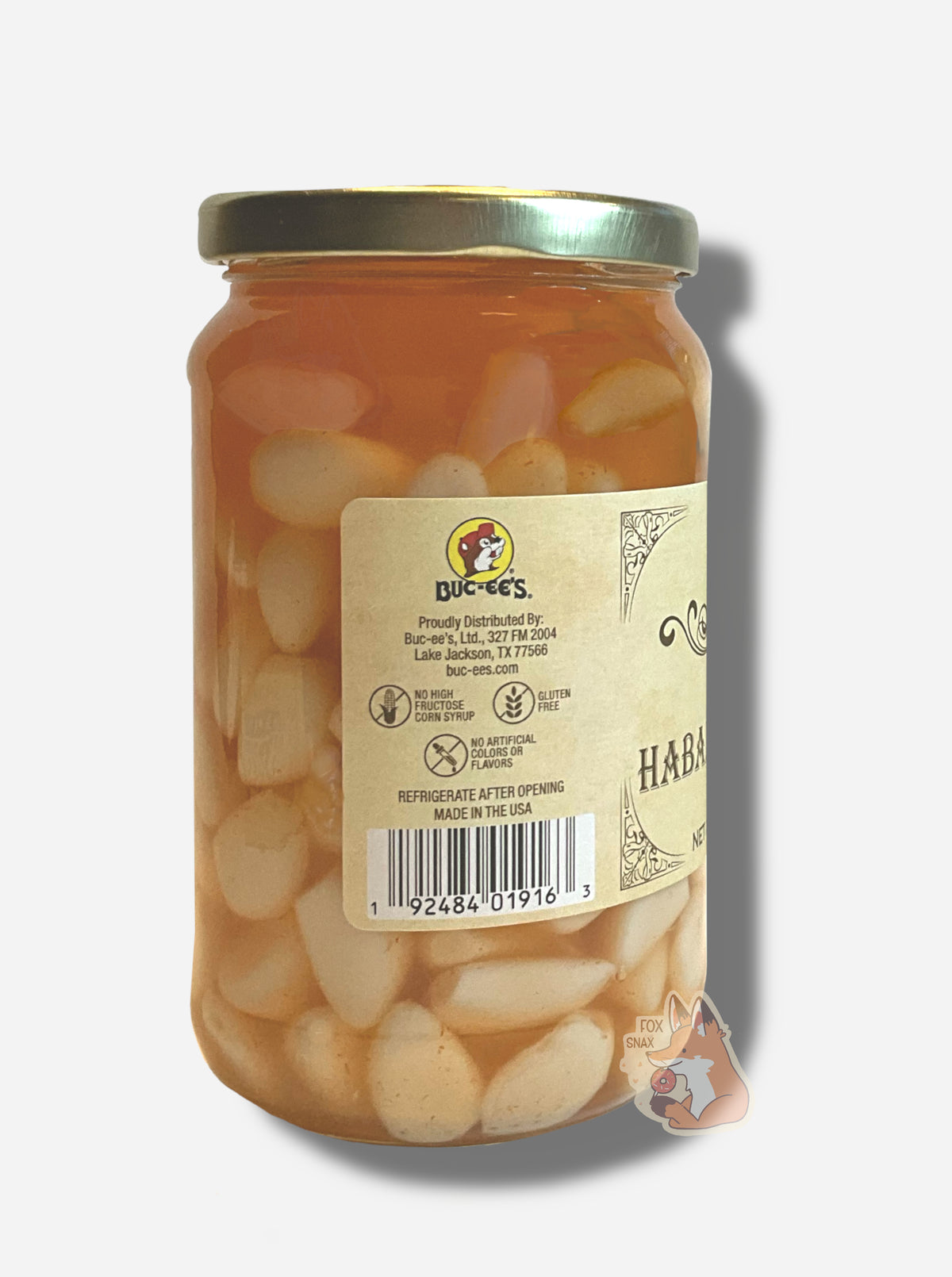 A picture of the left side of a glass jar of Buc-ee's Pickled Habanero Garlic - the label is a "old-timey" sort of white/yellow with flared edges. The middle reads No High Fructose Corn Syrup, No Artificial Colors Or Flavors, Gluten Free. In the jar, garlic gloves floating in orange habanero pepper brine can be seen.