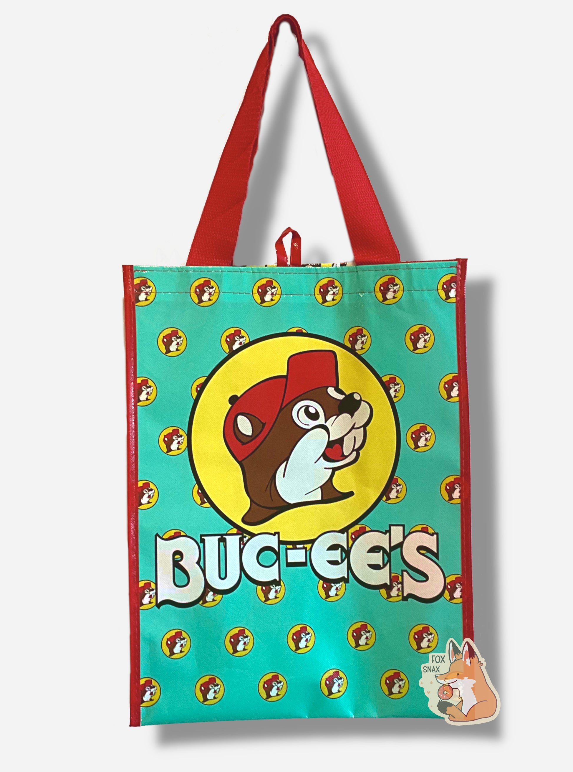 A picture of a large rectangular turquoise plastic shopping bag with multiple small Buc-ee The Beaver logos on it.  The bag itself has a large Buc-ee's logo right in the middle and the word BUC-EE'S in white text underneath of it.  The strap on the bag is made of red  cloth. The vertical edges of the bag have a thin red stripe.