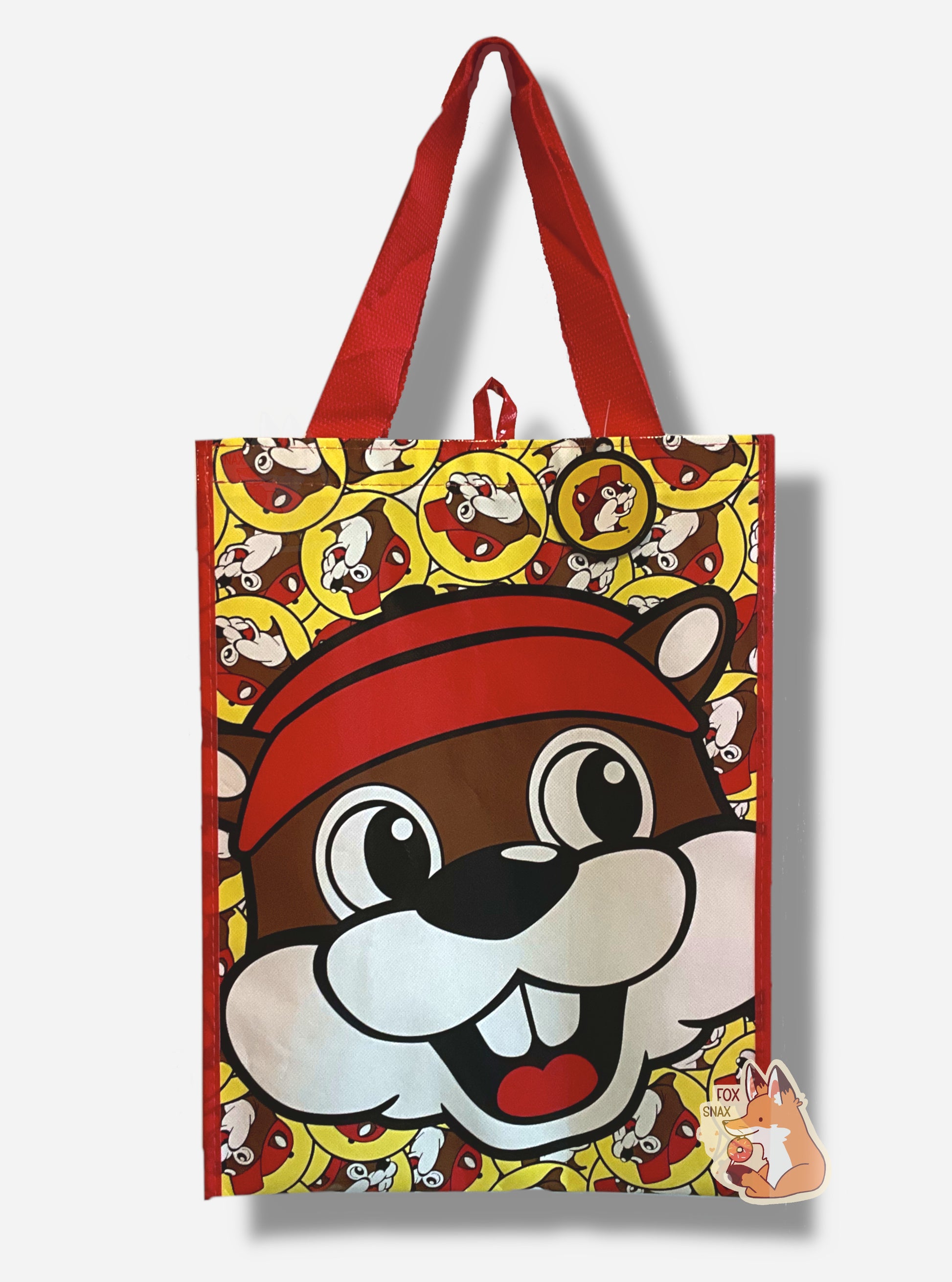 A picture of a large rectangular red plastic shopping bag with the multiple Buc-ee The Beaver logos on it.  The bag itself has a large closeup of Buc-ee's face right in the middle.   The strap on the bag is made of red  cloth.  The vertical edges of the bag have a thin red stripe.