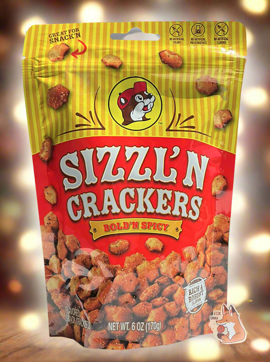 A picture of a metallic bag of Buc-ee's Sizzl'n Crackers and Bold'N Spicy. The logo is a dark red background on white text; a large number of reddish, savory-looking hexagonal oyster crackers are shown beneath it. At the top is a picture of the logo of Buc-ee The Beaver, and it reads GREAT FOR SNACK'N, NO ARTIFICIAL COLORS, NO ARTIFICIAL PRESERVATIVES, NO ARTIFICIAL FLAVORS and RICH AND ROBUST FLAVOR. The background shows many bright lights framing the bag.