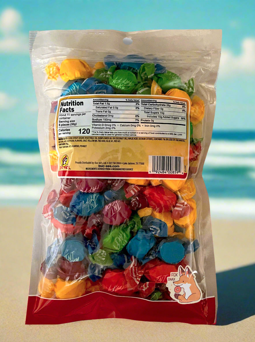 A picture of the back of a plastic bag of Buc-ee's Sour Salt Water Taffy. The bag is clear plastic. Inside it, twists of candy in five different wrapping colors (red, yellow, green, purple) can be seen. The background is of a tan beach, with green/blue ocean waves, against a blue sky.