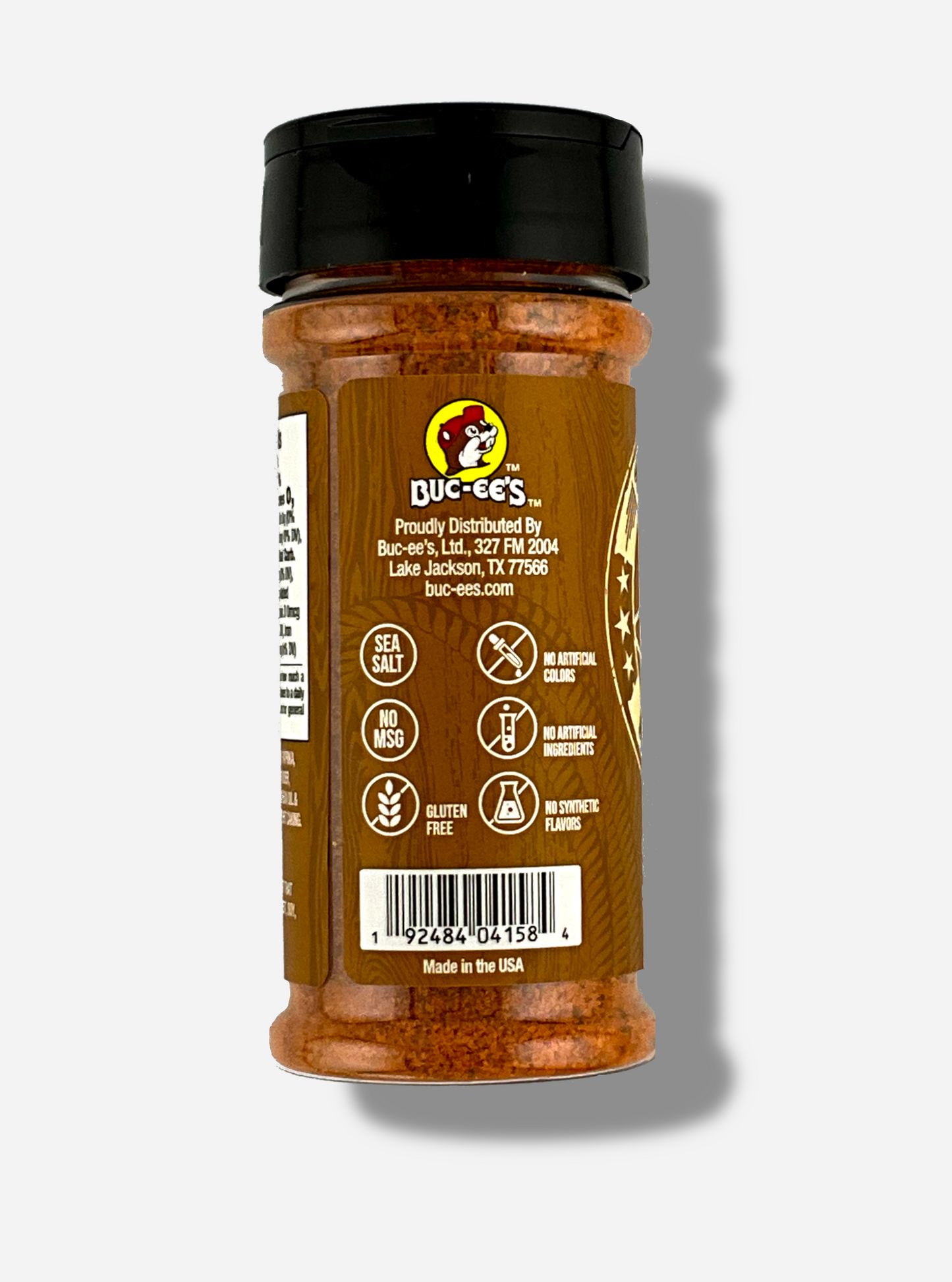 A picture of the side of a container of Texas Round Up Steak Seasoning. The container has a black plastic flip lid, and a clear plastic body. The spices inside appear orange and black. The tan label reads SEA SALT, NO MSG, GLUTEN FREE, NO ARTIFICIAL COLORS, NO ARTIFICIAL INGREDIENTS, NO SYNTHETIC FLAVORS. Beneath that, MADE IN THE USA.