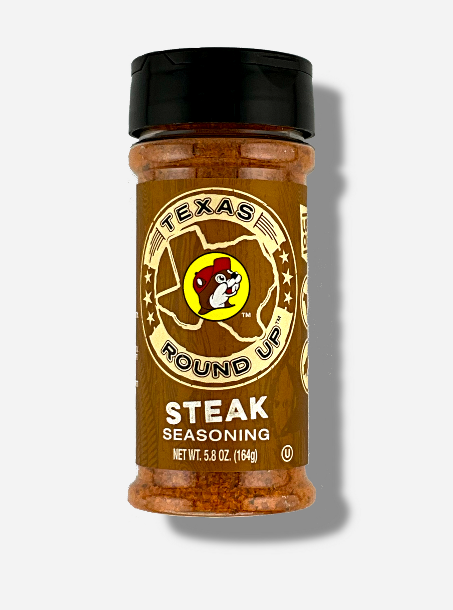 A picture of the front of a container of Texas Round Up Steak Seasoning. The container has a black plastic flip lid, and a clear plastic body. The spices inside appear red/orange and black. The label reads TEXAS ROUND UP, with an outline of the state of Texas, with a picture of Buc-ee The Beaver in the middle. Beneath that, the tan label reads in white text, Steak Seasoning. Net Wt 5.8 Oz (164g).