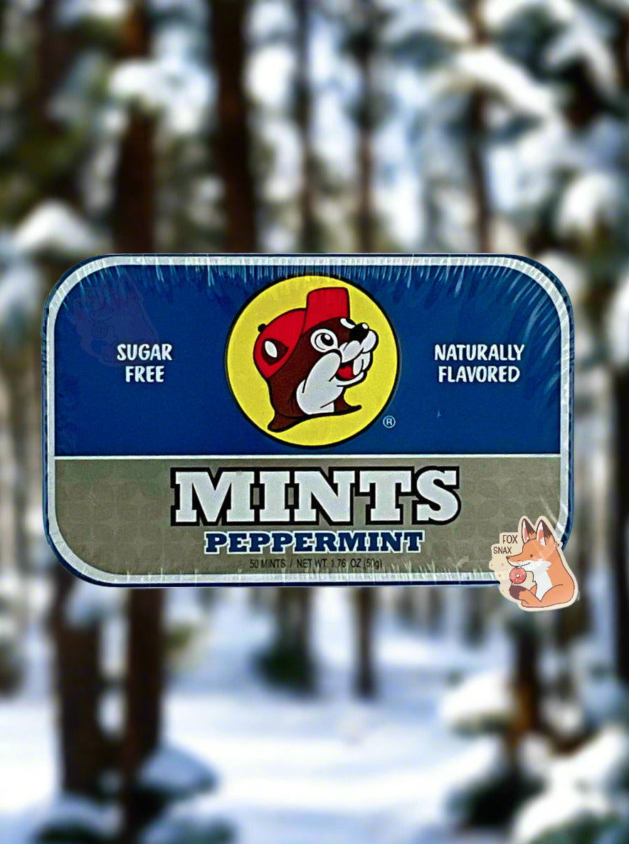 A picture of a tin of Buc-ees Peppermint Mints. The cover is decorated with a big picture of Buc-ee The Beaver, and has a dark blue and silver background. The tin reads Sugar Free, Naturally Flavored, Mints, Peppermint. The background shows a snowy, forested winter wonderland, covered in pine trees.