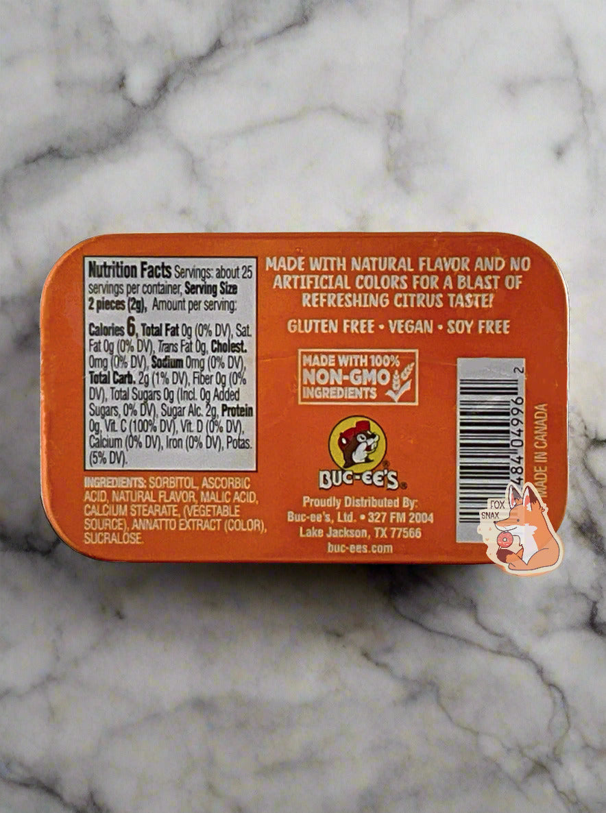 A picture of a back of a tin of Buc-ees Orange Blast Sours. The back cover is decorated with a small picture of Buc-ee The Beaver, and has the following text: Made With Natural Flavor And No Artificial Colors For A Blast Of Refreshing Citrus Taste!, Gluten Free, Vegan, Soy Free, made with 100% Non-GMO Ingredients. The tin is sitting on a beautiful grey and black quartz countertop.