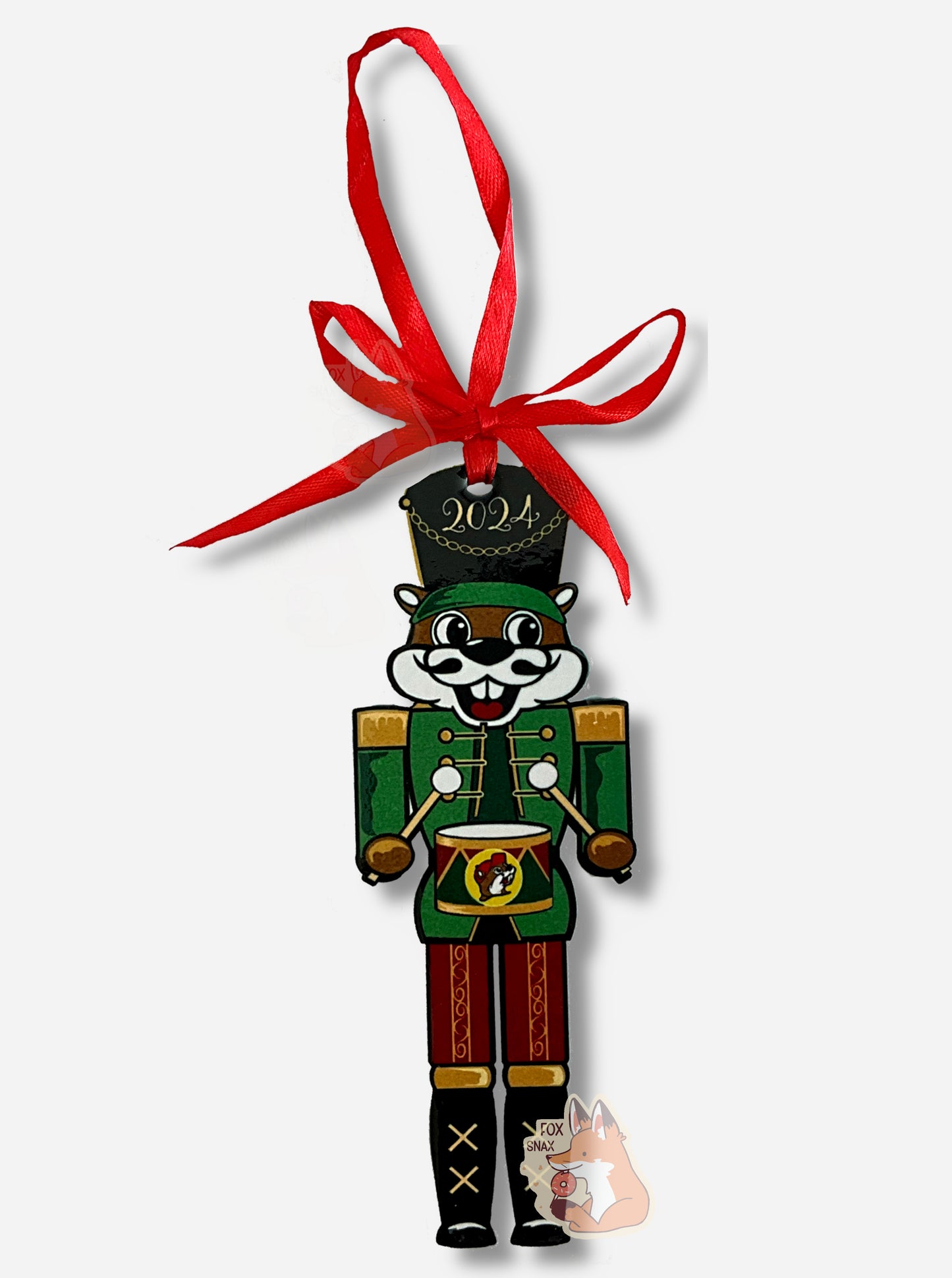 A picture of Buc-ee the Beaver, dressed as a nutcracker. Buc-ee's hat is a large black one and has 2024 on it. In each hand, he is holding a drumstick, and a small drum (with a Buc-ee's logo) in green in red is at his waist. His legs are covered in ornate red pants with gold trim; his boots are large and black. His vest is green with yellow buttons. His smile is framed with a black mustache.