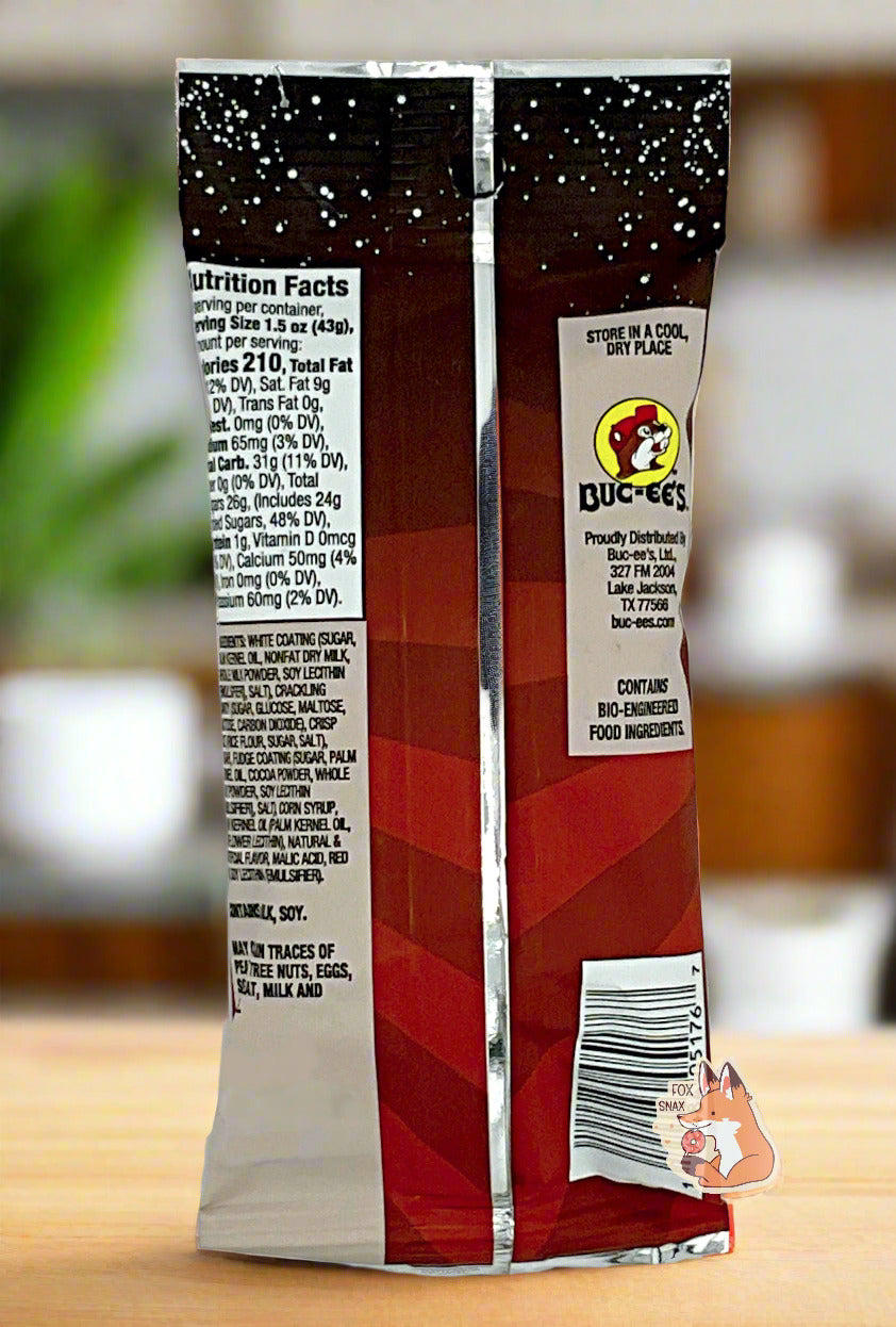 A picture of the back of a bag of Buc-ee's Cosmic Pops, in Cherry Cola flavor. The back of the bag reads STORE IN A COOL, DRY PLACE, then shows a picture of the Buc-ee's beaver logo, then CONTAINS BIO-ENGINEERED FOOD INGREDIENTS. The background is of a bright cheery kitchen; the bag is resting on a wooden countertop.