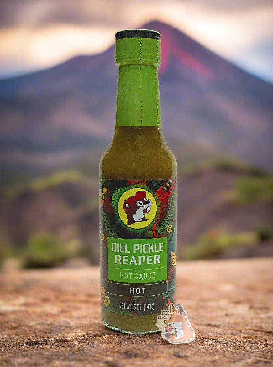 A picture of a small, tall glass bottle of hot sauce. The top of the bottle is sealed with a green plastic cover on a black cap. The front label of the bottle reads DILL PICKLE REAPER, HOT. The Buc-ee's logo can be seen on the front; the background is a fairly busy abstract artwork featuring several pickles and chilis. The sauce inside is a green/yellow with smaller green dots. In the background is an angry volcano, complete with lava.