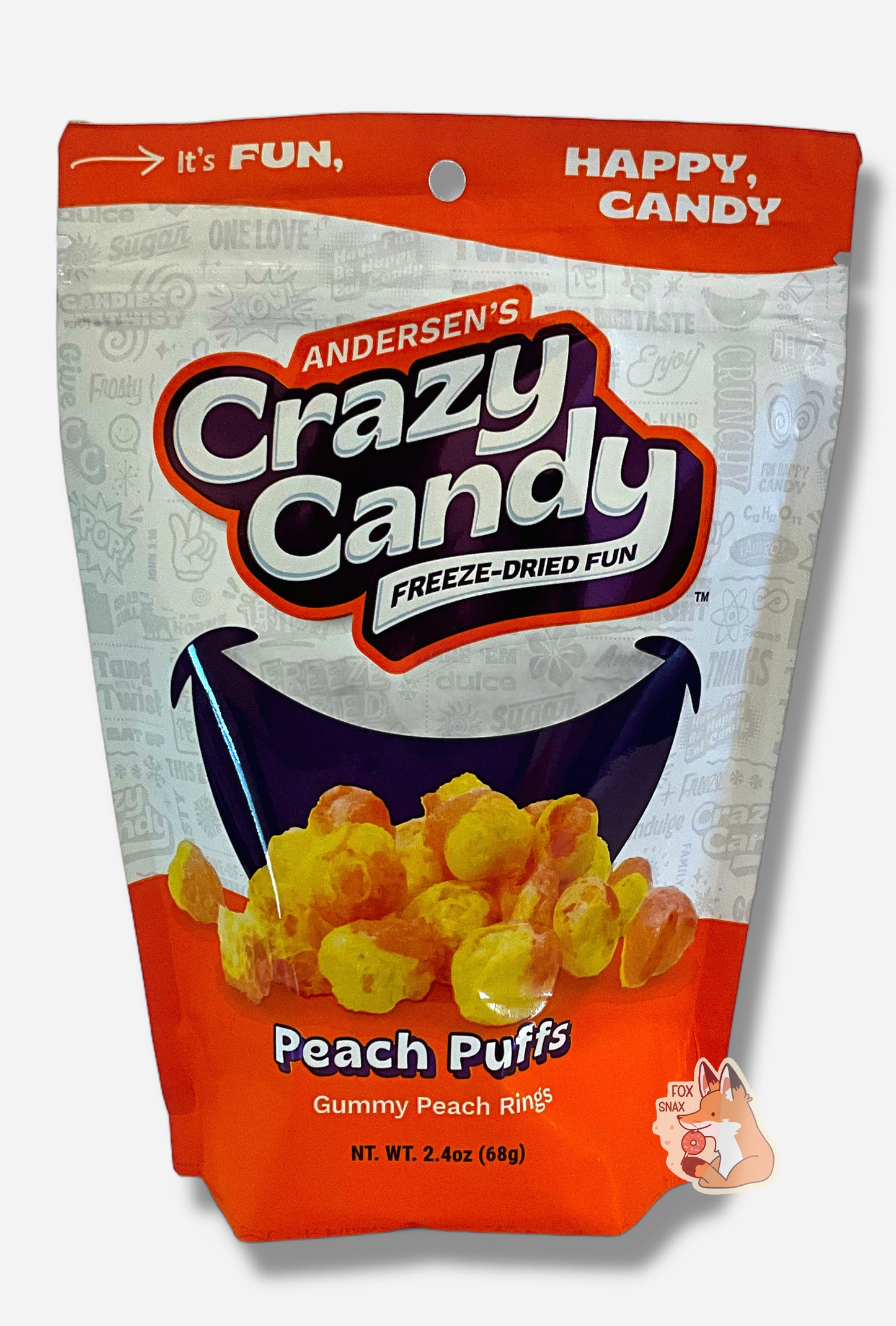 A large bag of Andersen's Peach Puffs. The front of the bag also says Gummi Peach Rings, Net Weight 2.4 oz. It's Fun, Happy, Candy. The top and bottom of the bag are orange, and the background is a large purple smile against a white background.