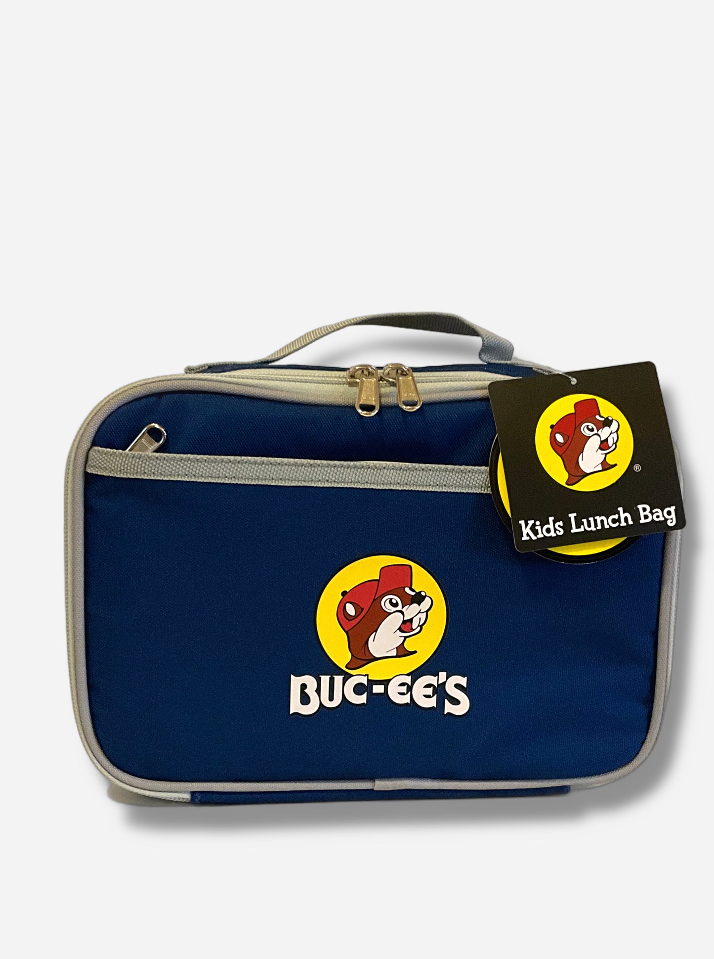 A picture of a front view of a children's lunch box. The outer surface is made of blue polyester, and has a small grey strap on the top. The front of the cooler has a picture of the Buc-ee's logo on it: a grinning beaver wearing a red hat against the background of a yellow circle. Underneath the logo reads BUC-EE'S in white text. The front of the lunch box has a small zip pocket. The top right of the lunch box has a paper tag that reads KIDS LUNCH BAG.