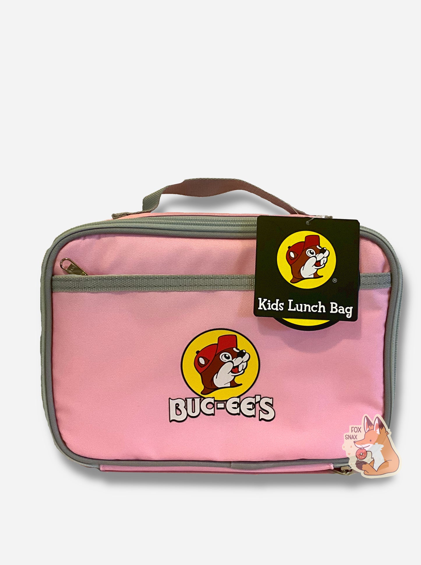 A picture of a front view of a children's lunch box. The outer surface is made of pink polyester, and has a small grey strap on the top. The front of the cooler has a picture of the Buc-ee's logo on it: a grinning beaver wearing a red hat against the background of a yellow circle. Underneath the logo reads BUC-EE'S in white text. The front of the lunch box has a small zip pocket. The top right of the lunch box has a paper tag that reads KIDS LUNCH BAG.