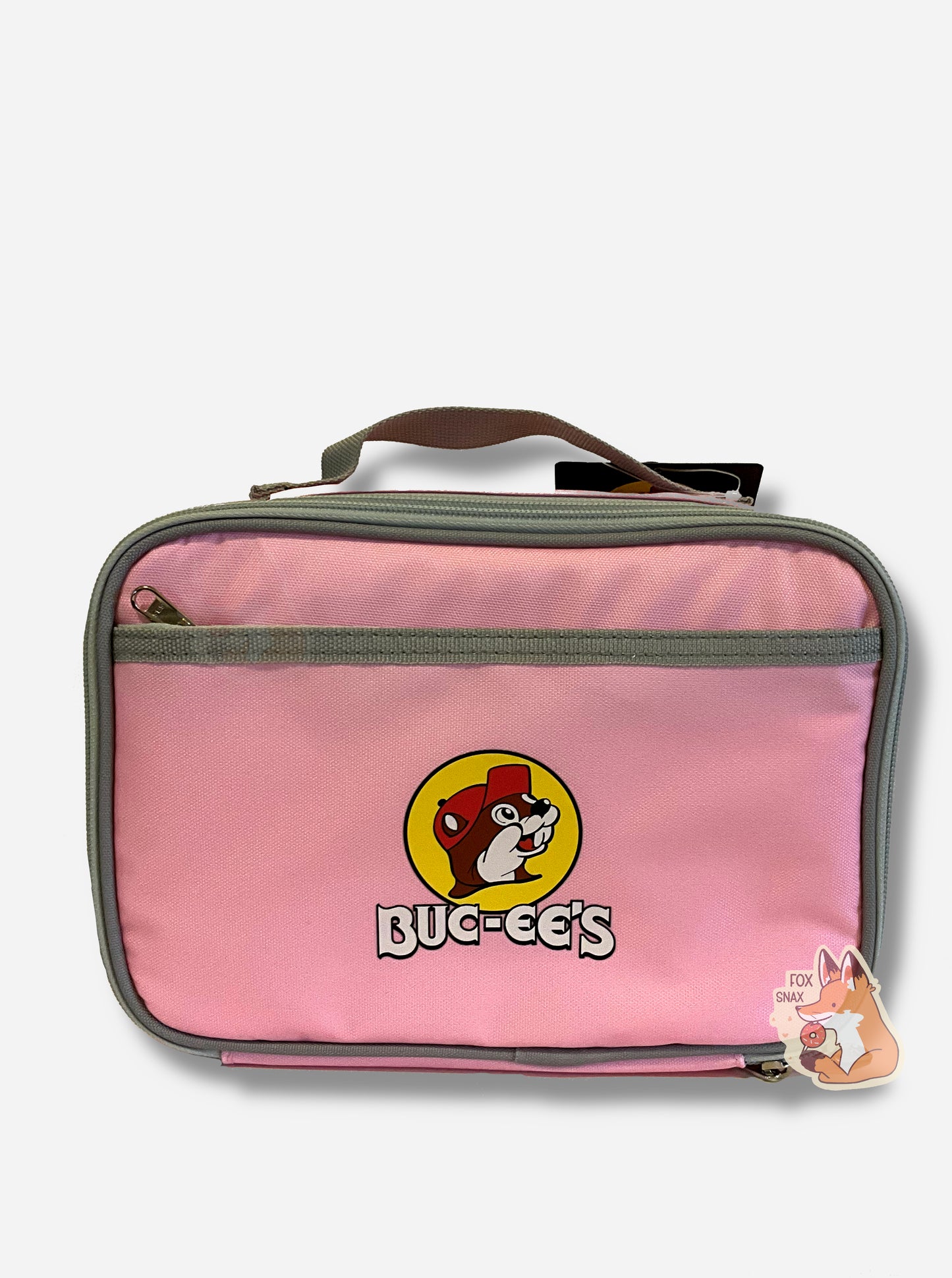 A picture of a front view of a children's lunch box. The outer surface is made of pink polyester, and has a small grey strap on the top. The front of the cooler has a picture of the Buc-ee's logo on it: a grinning beaver wearing a red hat against the background of a yellow circle. Underneath the logo reads BUC-EE'S in white text. The front of the lunch box has a small zip pocket.
