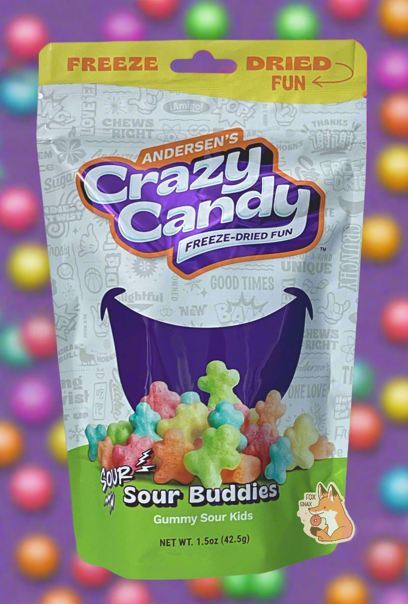 A large bag of Andersen's Sour Buddies The front of the bag also says Gummy Sour Kids, Net Weight 1.5 oz. The top of the bag is yellow, and in red text says "FREEZE DRIED FUN". The middle bottom of the bag shows a large series of puffy, red, orange, yellow, green and blue figures, and the background is a large dark blue smile against a white background with text. The background shows a purple background with a variety of brightly colored candy dots.