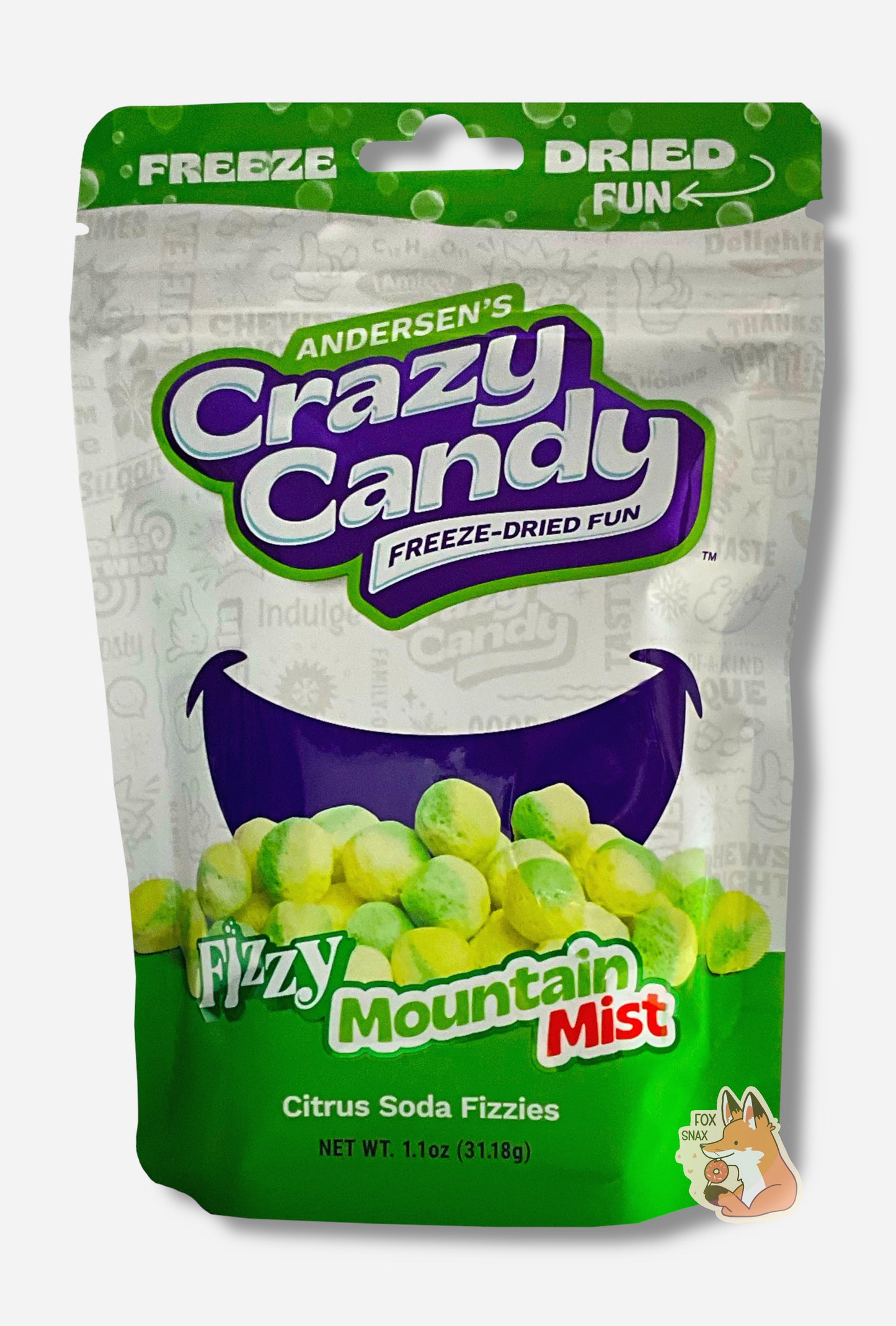 A large bag of Andersen's Fizzy Mountain Mist. The front of the bag also says Citrus Soda Fizzies, Net Weight 1.1 oz. It's Fun, Happy, Candy. The top and bottom of the bag are green, and the background is a large dark blue smile against a white background.