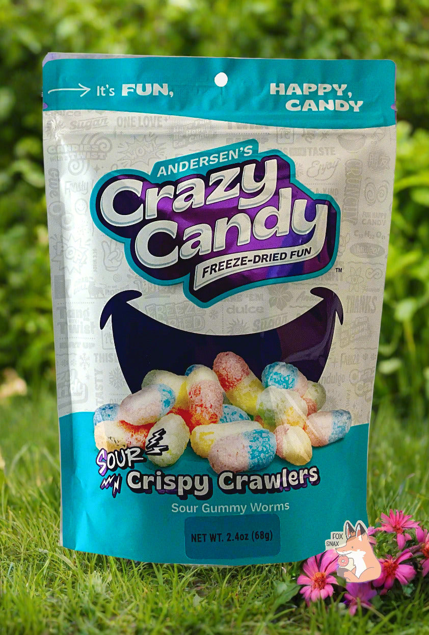 A large bag of Andersen's Sour Crispy Crawlers. The front of the bag also says Sour Gummy Worms, Net Weight 2.4 oz. It's Fun, Happy, Candy. The top and bottom of the bag are light blue, and the background is a large dark blue smile against a white background. The background is of a pretty flower garden, with pink coneflowers.
