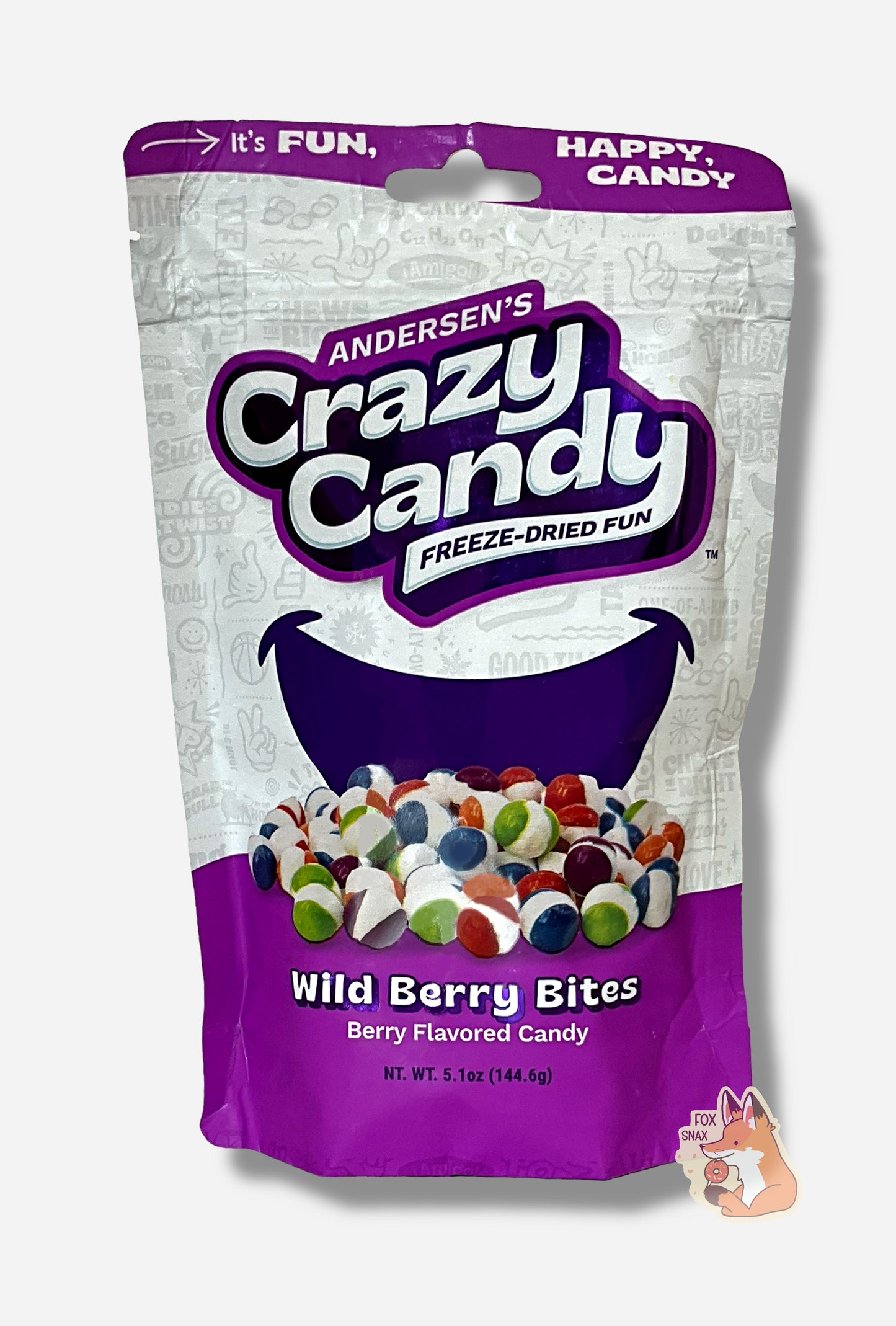 A large bag of Andersen's Wild Berry Bites. The front of the bag also says Berry Flavored Candy, Net Weight 5.1 oz. It's Fun, Happy, Candy. The top and bottom of the bag are light purple, and the background is a large purple smile against a white background.