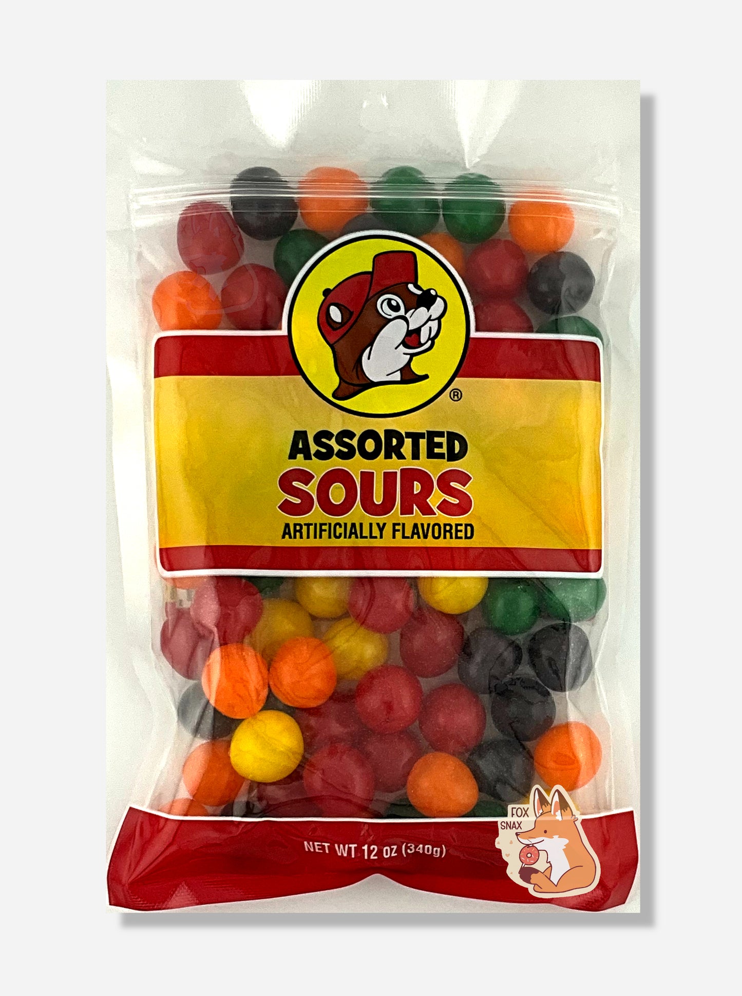A picture of the front of a resealable bag of Buc-ee's Assorted Sours, which are sour and sweet candies. The bag reads ASSORTED SOURS, Artificially Flavored, and has a picture of Buc-ee the Beaver on it. The sours inside are spherical, and are multiple shades of red, orange, yellow, green, and purple.