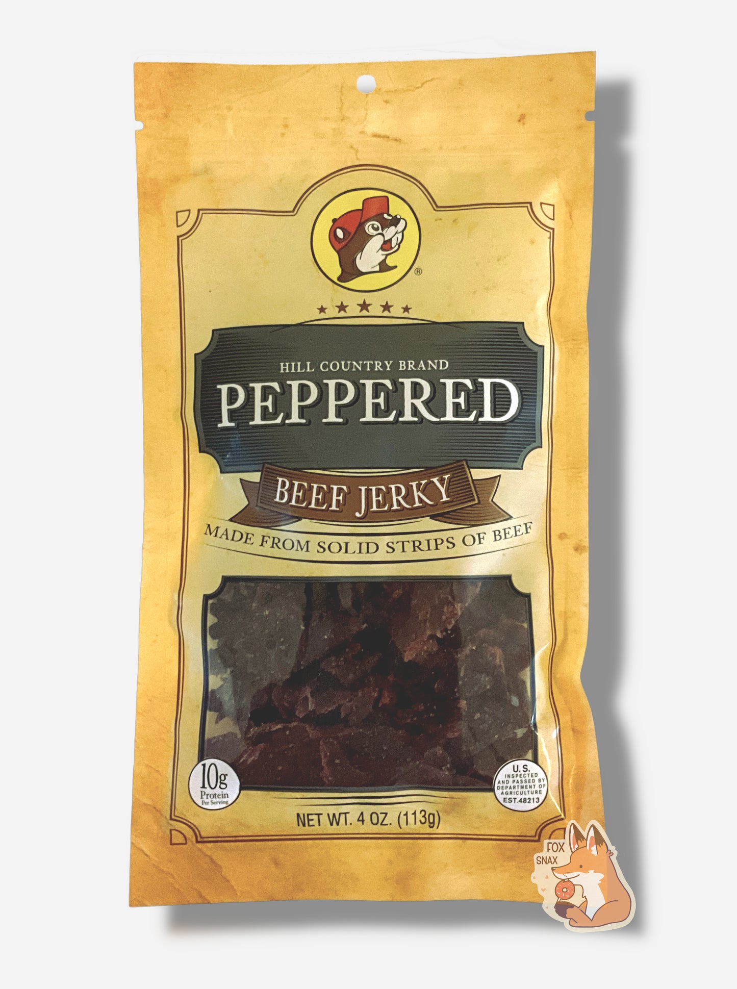 A picture of the front of a tan plastic bag of Buc-ee's Hill Country Brand Peppered Beef Jerky. The logo is in dark grey with white text. The label underneath reads 'Made From Solid Strips Of Beef'.A small window on the bottom of the bag shows the dark brown/red dried jerky inside. The bag has a picture of Buc-ee the Beaver on it.