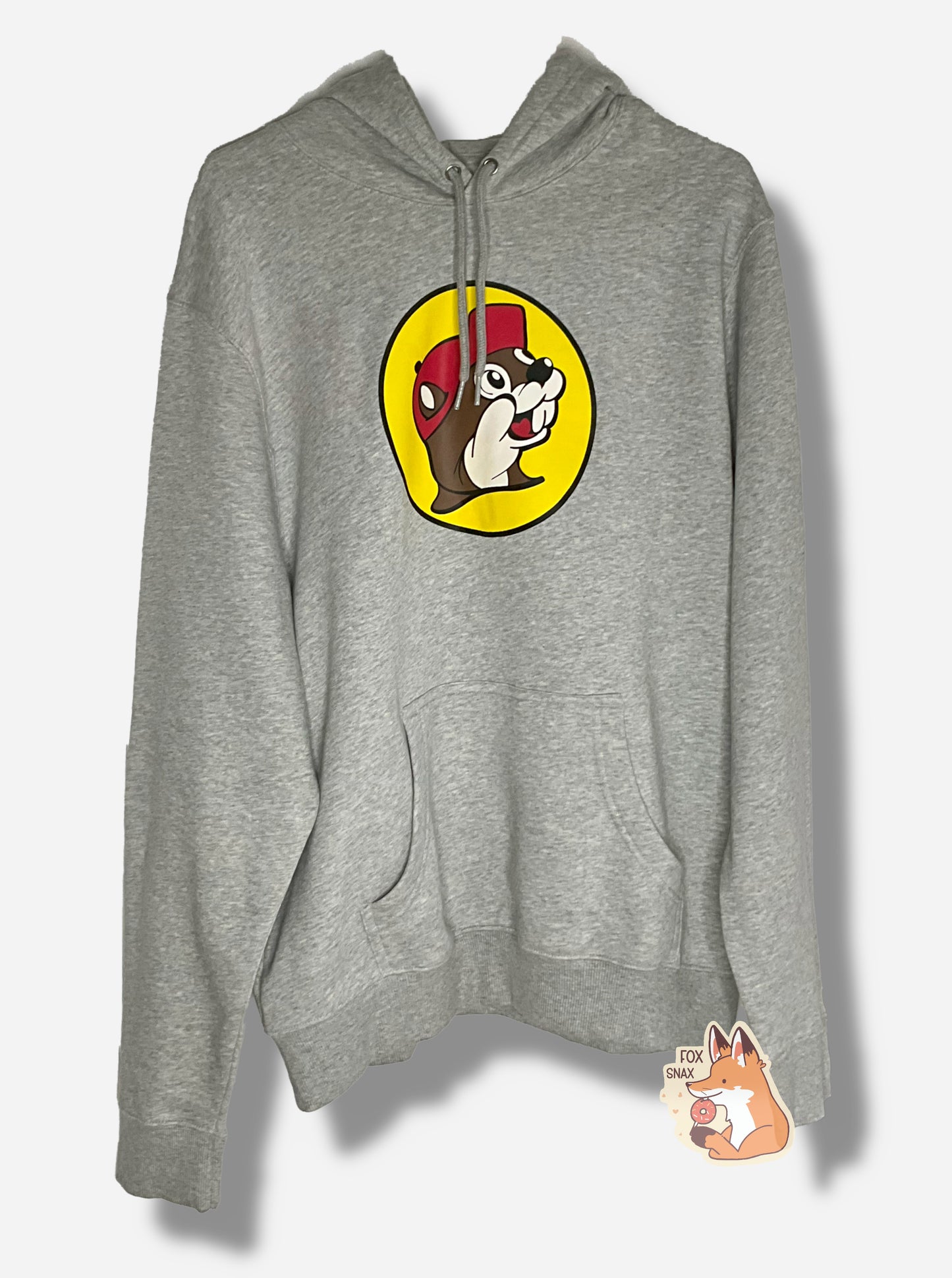 A picture of a grey cotton/polyester hoodie sweatshirt. The dead center of the shirt shows the Buc-ee's logo: a jolly, brown and white furred beaver with a grin and a significant overbite, wearing a red ball cap, against the background of a yellow circle. The bottom of the hoodie has a spot for warming one's hands, the neck has a drawstring to pull the opening of the hoodie tighter.