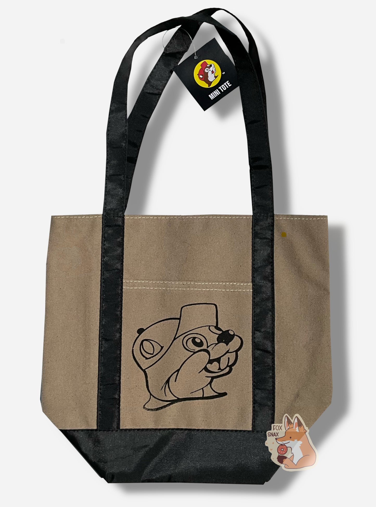 Picture of the back of a small tote bag, with shiny black cloth straps. In the center of the bag is a black outline of Buc-ee The Beaver: a jolly beaver wearing a ballcap and a buc-toothed smile.