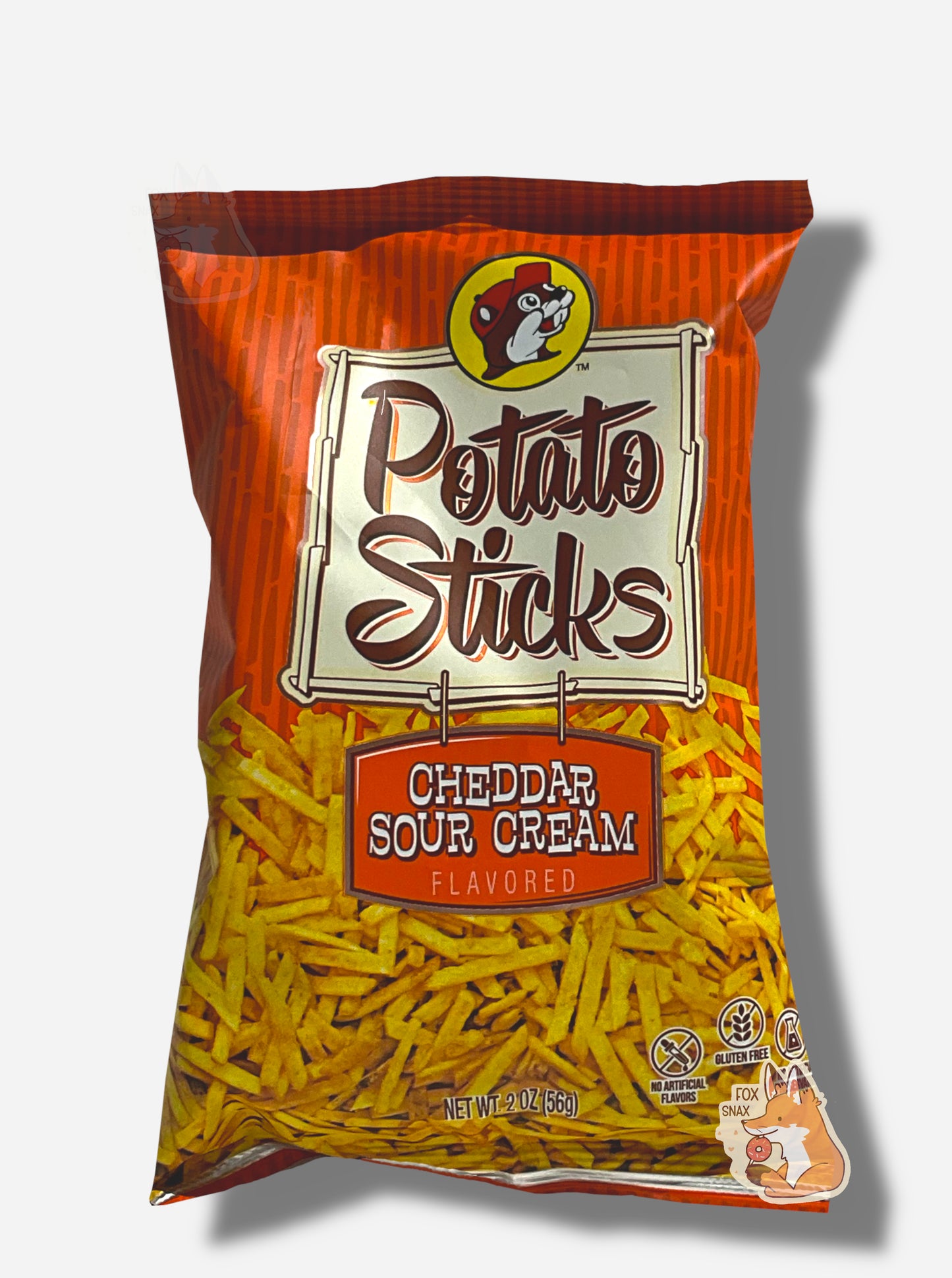 A bag of Buc-ee's Cheddar Sour Cream Flavored Potato Sticks. The bag is in dark and light red and has a white sign in the middle in black text that reads POTATO STICKS, then under that, CHEDDAR SOUR CREAM FLAVORED. A large number of skinny (skinnier than french fries) potato sticks frame the bottom of the bag.
