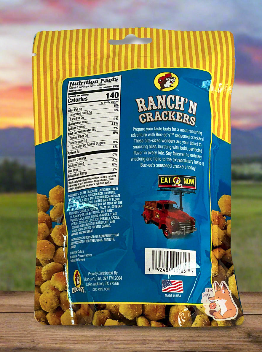 A picture of a the back of a metallic bag of Buc-ee's Ranch'N Crackers. It reads "Prepare your taste buds for a mouthwatering adventure with Buc-ee's TM seasoned crackers! These bite-sized wonders are your ticket to snacking bliss, bursting with bold, perfected flavor in every bite. Say farewell to ordinary snacking and hello to the extraordinary taste of Buc-ee's seasoned crackers today! The background is of a meadow, framed against a beautiful multicolored sunset.