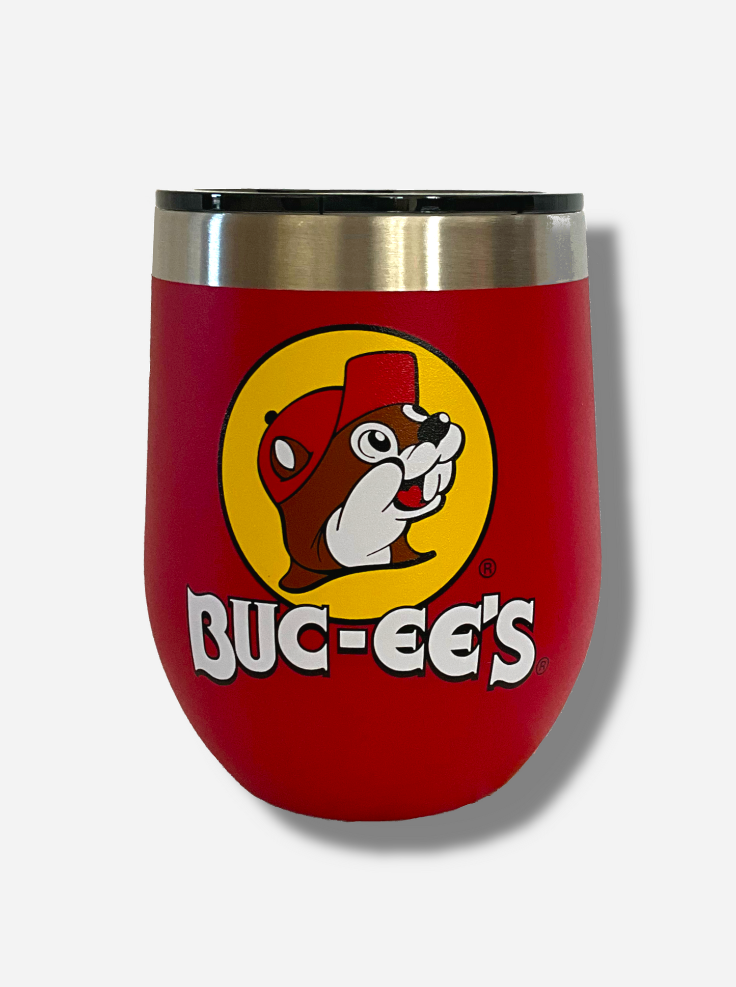 A picture of a short, red, sorta squatty tumbler, with a big picture of Buc-ee The Beaver on it. Underneath the picture is the BUC-EE'S logo. The surface is smooth and red, as it is red paint covering stainless steel. The top of the tumbler and a slider on top to open and close it are plastic. The top of the tumbler is lined with a stainless steel band.