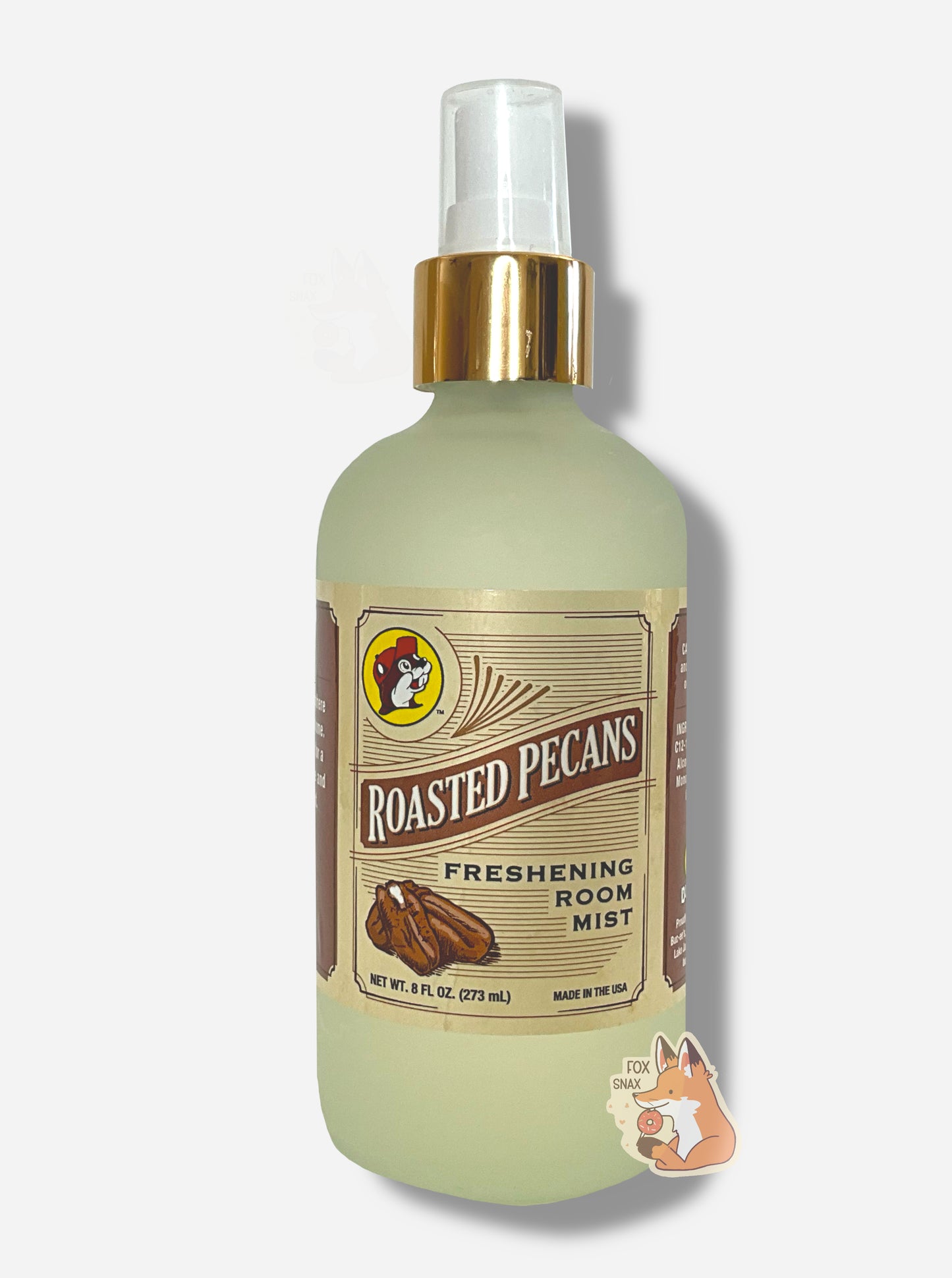 Front of a spray bottle of Buc-ee's Roasted Pecans Freshening Room Mist on a white background. The bottle is frosted glass with a white sprayer and gold label, and has the Buc-ee's logo in the top left. The rest of the label has a series of brown lines, and reads ROASTED PECANS, then FRESHENING ROOM MIST, then NET WT 8 FL OZ, then MADE IN THE USA.
