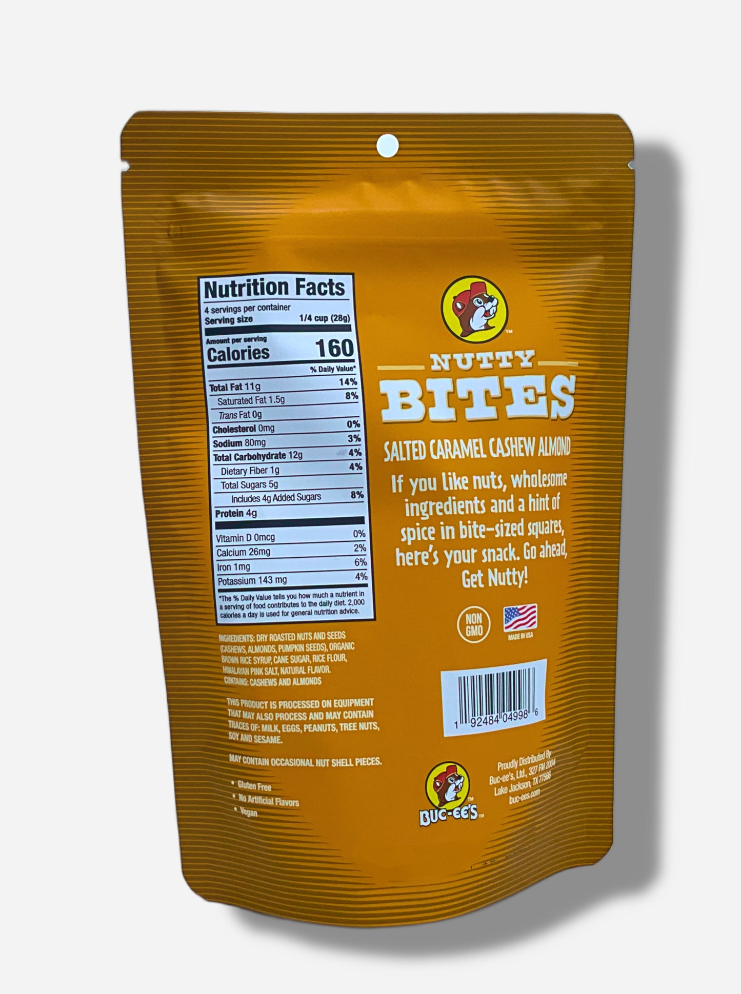 A picture of the back of a orange and white bag of Buc-ee's Salted Caramel Cashew Almond Nutty Bites. The Buc-ee's logo can be seen in the top right of the bag, then under that, NUTTY BITES, then SALTED CARAMEL CASHEW ALMOND, then "If you like nuts, wholesome ingredients and a hint of spice in bite-sized squares, here's your snack. Go ahead and Get Nutty!" Nutrition facts and ingredients are listed as well.