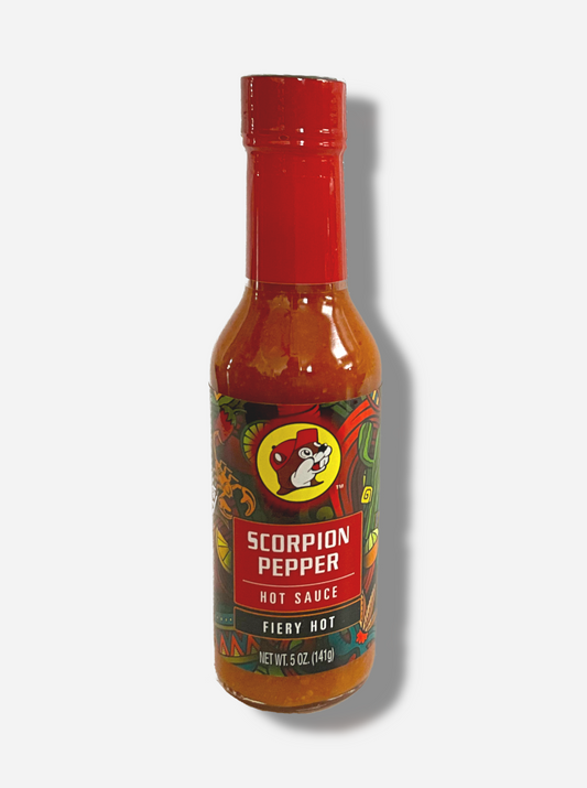 A picture of a small, tall glass bottle of hot sauce.  The top of the bottle is sealed with a plastic top.  The front label of the bottle reads SCORPION PEPPER HOT SAUCE, HOT.  The Buc-ee's logo can be seen on the front; the background is a fairly busy abstract artwork featuring a scorpion, a lemon, a taco, and a maracas.  The sauce inside is an orange/red.