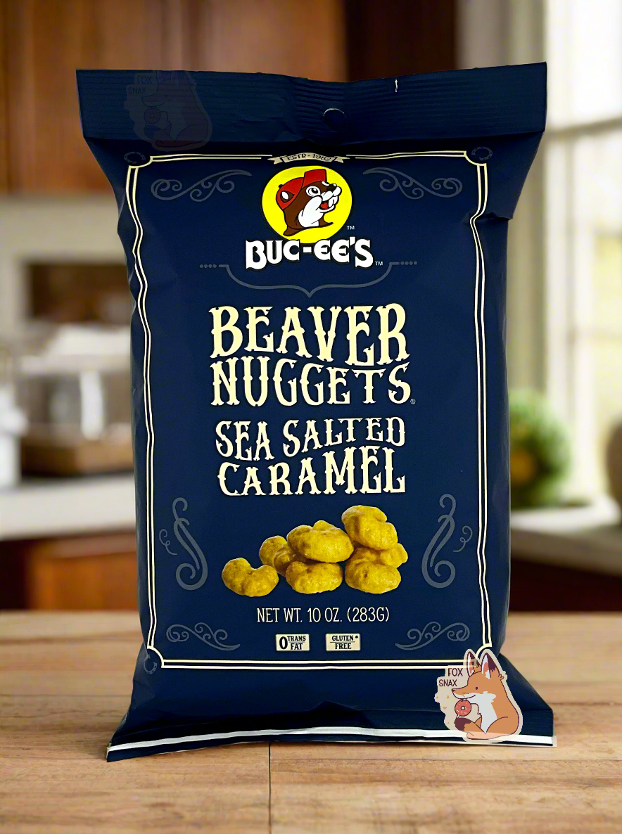 A picture of the front of a opaque, dark blue bag of Buc-ee's Beaver Nuggets, Sea Salted Caramel, which are puffed corn snack with caramel flavors. It has a picture of Buc-ee the Beaver on the top. The bag reads: 0 Trans Fat. Gluten Free. The nuggets are sitting on a wooden kitchen countertop.