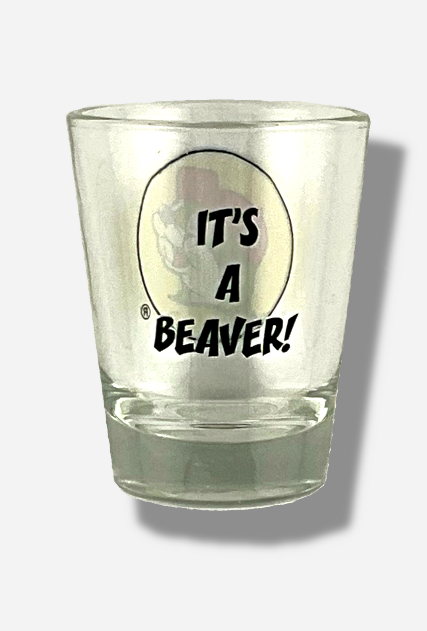 A picture of the back of glass shot glass. The glass is clear. In the middle of the back are the words, in black front, IT'S A BEAVER!