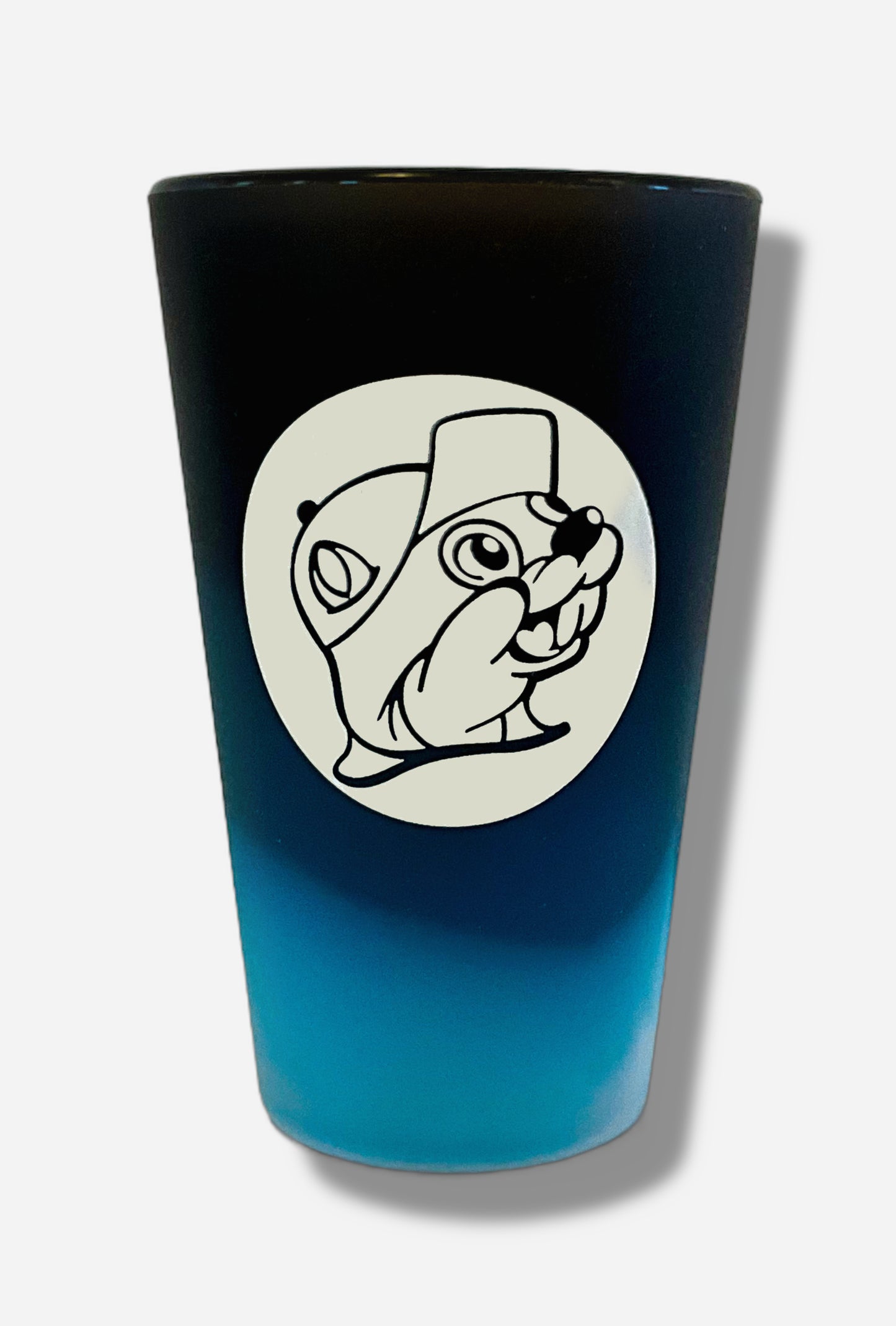 A picture of the front of silicone pint glass. The glass is a very light blue at the bottom, and via a "cloud-like" gradient, transitions to dark blue at the top. On front is the Buc-ee's logo in white; it is a cheerful beaver wearing a ballcap, against a white circle background.